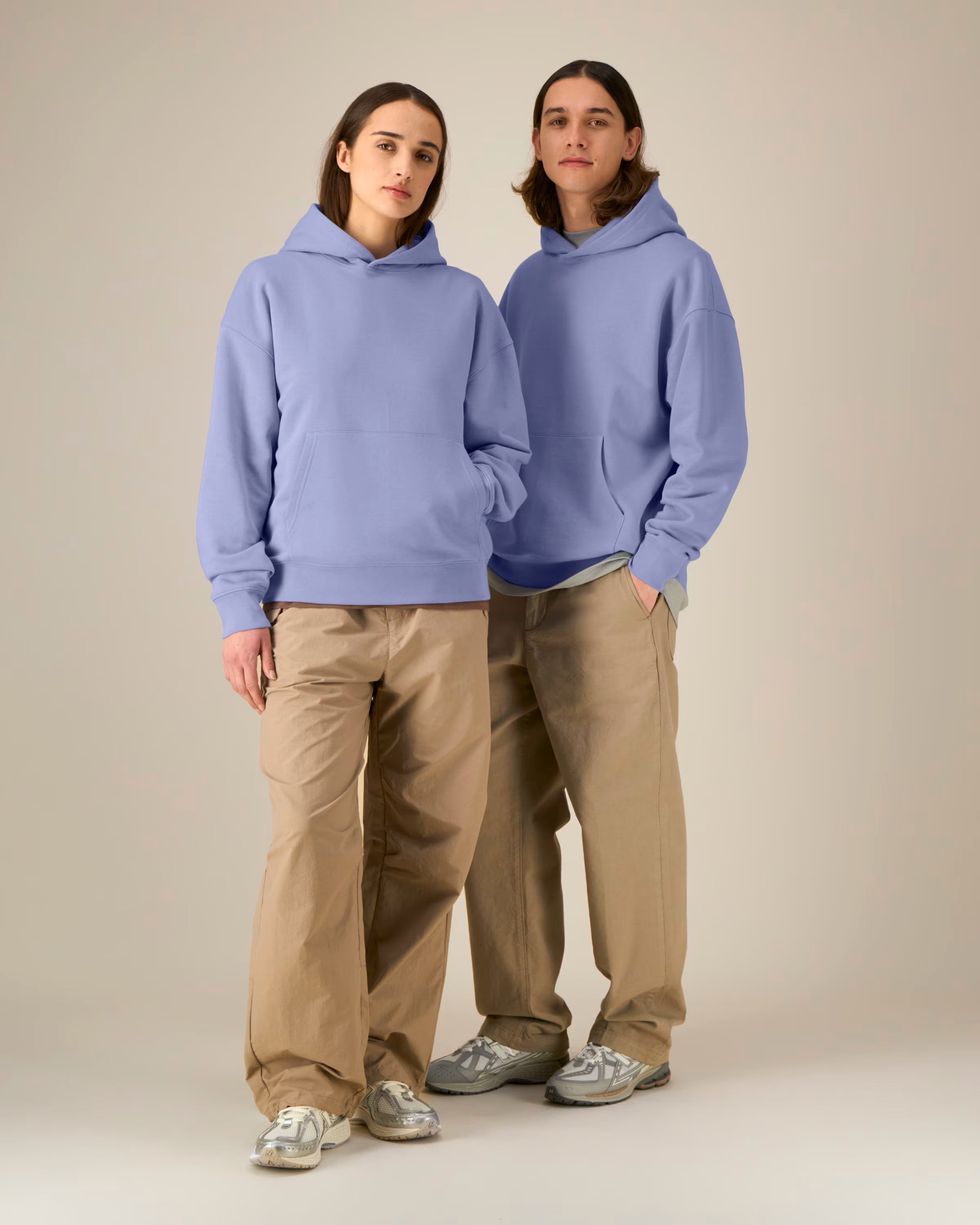 Two people wearing matching light blue unisex cotton hoodies and beige pants on a plain background