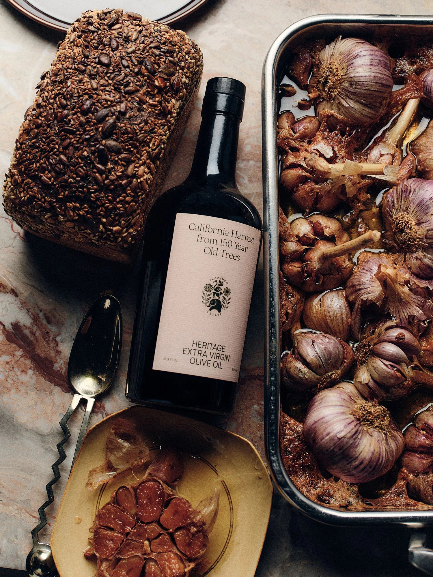 Bottle of olive oil with bread, roasted garlic, and cured meats on a stone surface