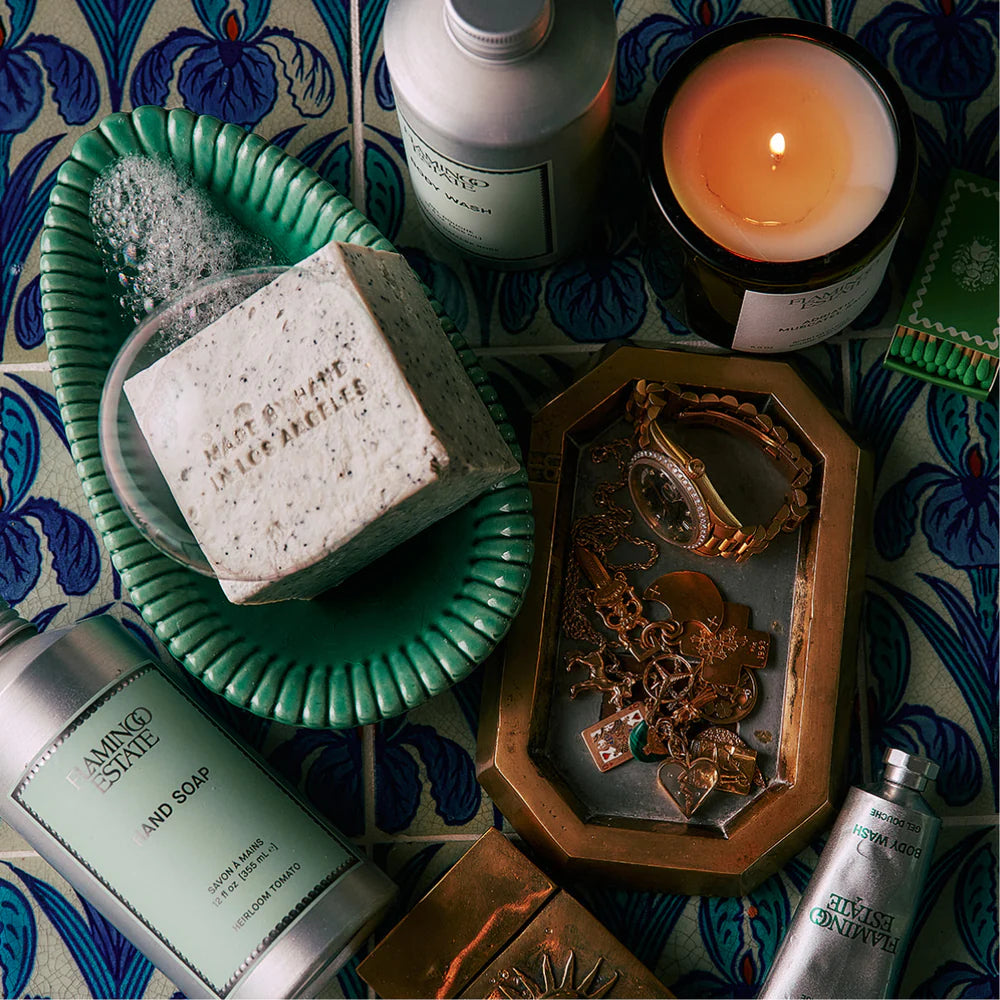 Cosmetic products including a bar of soap, bottles, and a candle on a decorative surface with blue and white patterns.