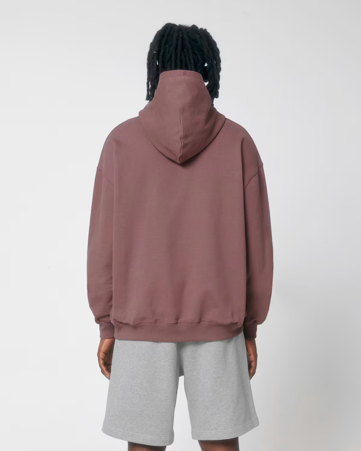 Back view of a female model wearing a dusty rose cotton hoodie in studio