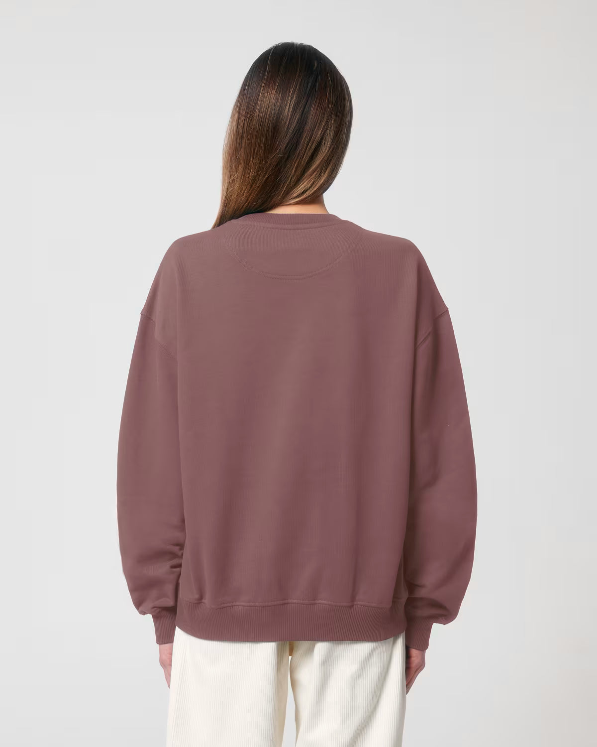 Back view of a female model wearing a dusty rose cotton hoodie in studio