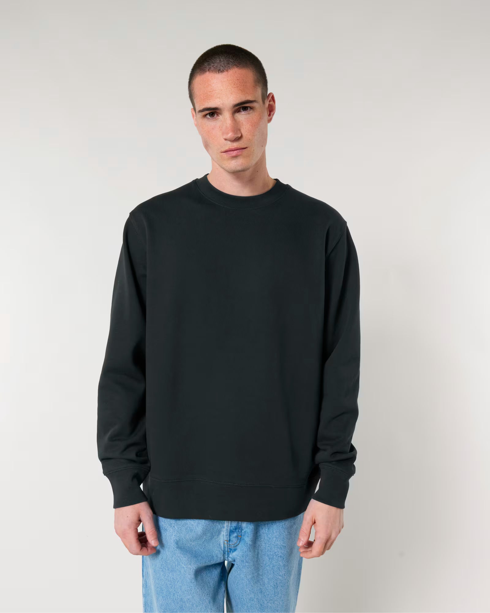 Man wearing a black unisex cotton sweatshirt and light blue jeans against a plain background