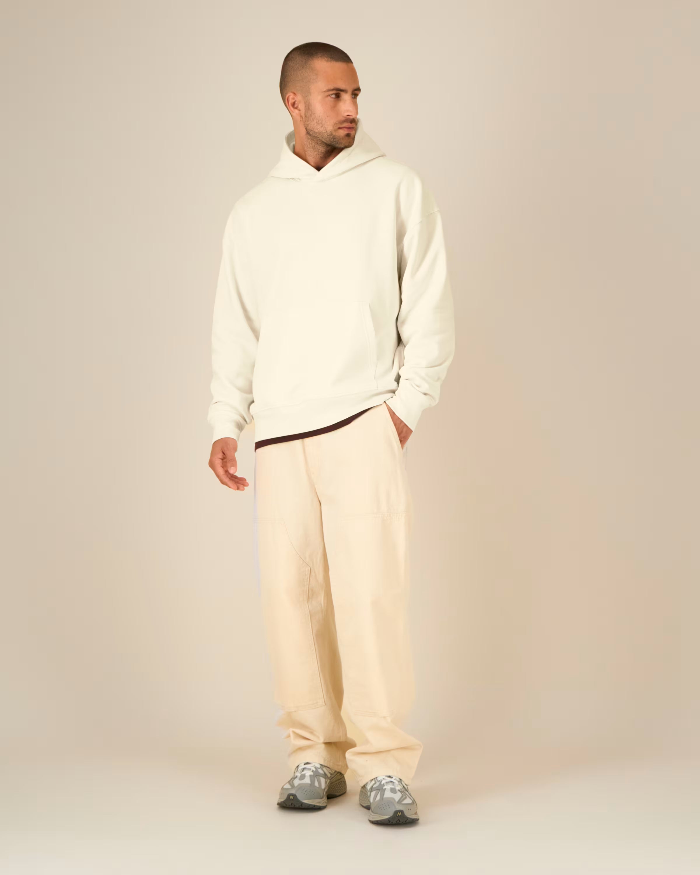 Man wearing a white unisex cotton hoodie and beige pants on a plain background