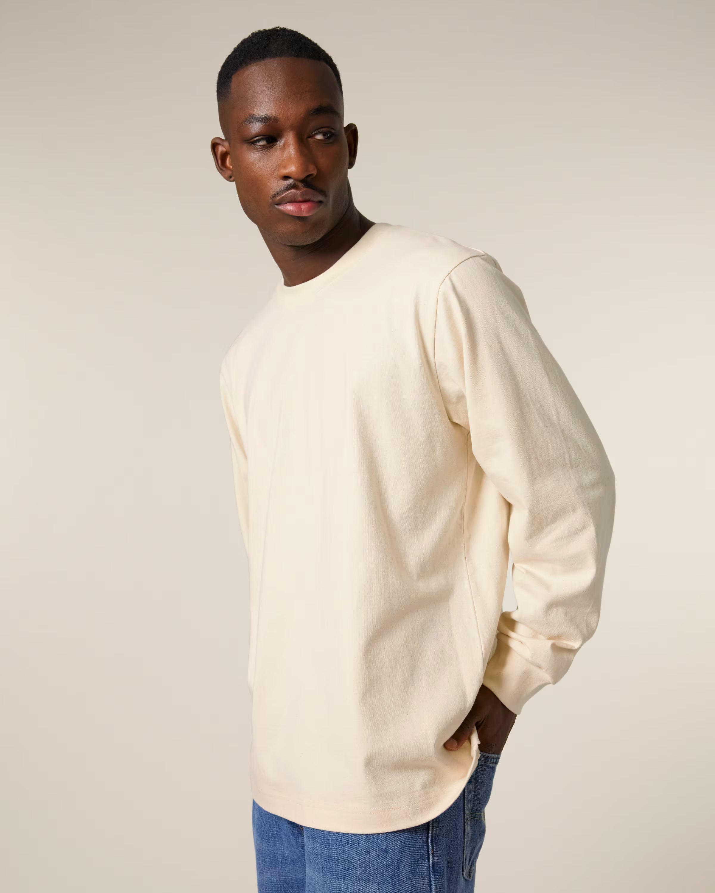 Man wearing a cream sunisex cotton weater and blue jeans against a plain background