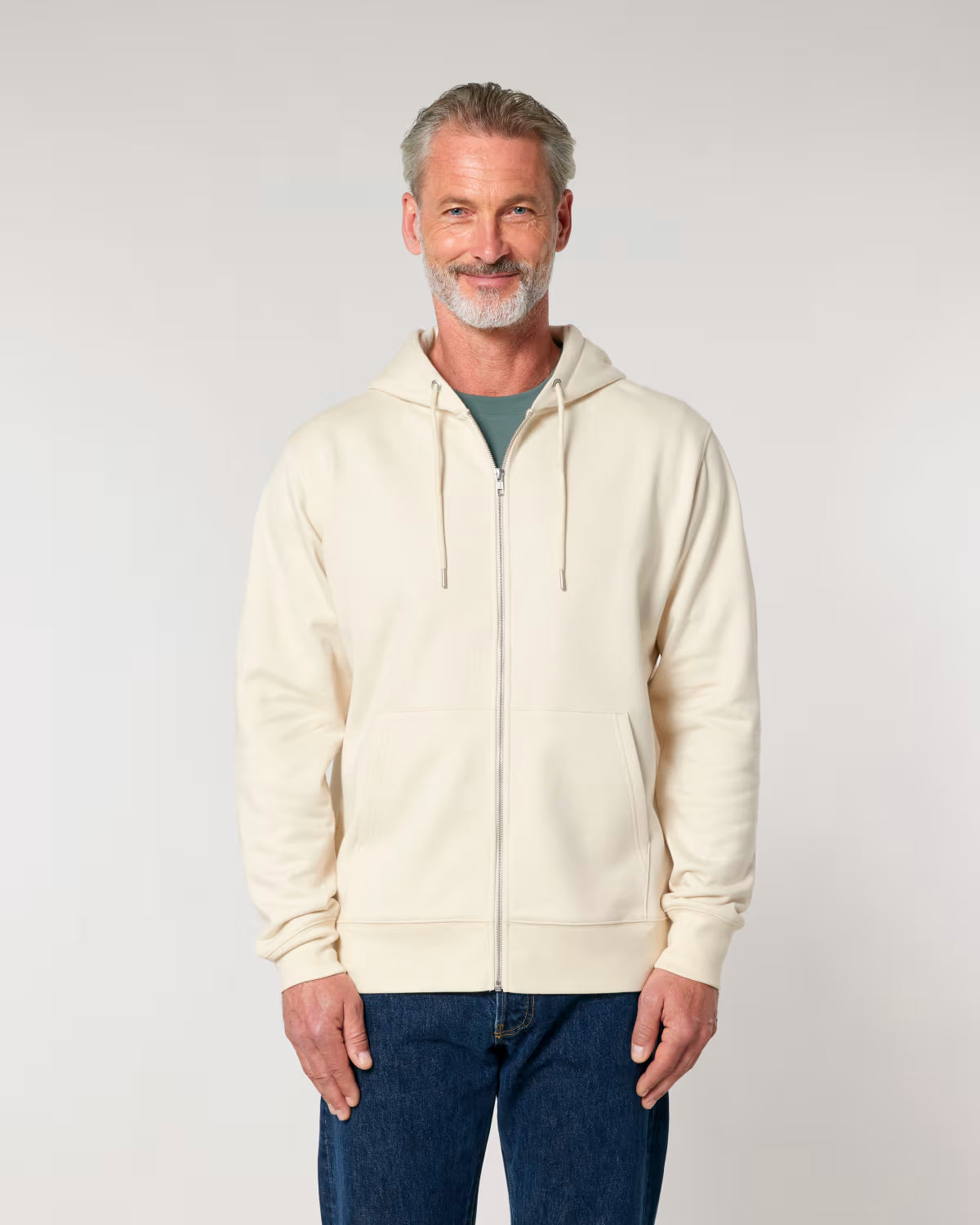 Man wearing a cotton cream hoodie and blue jeans against a white background