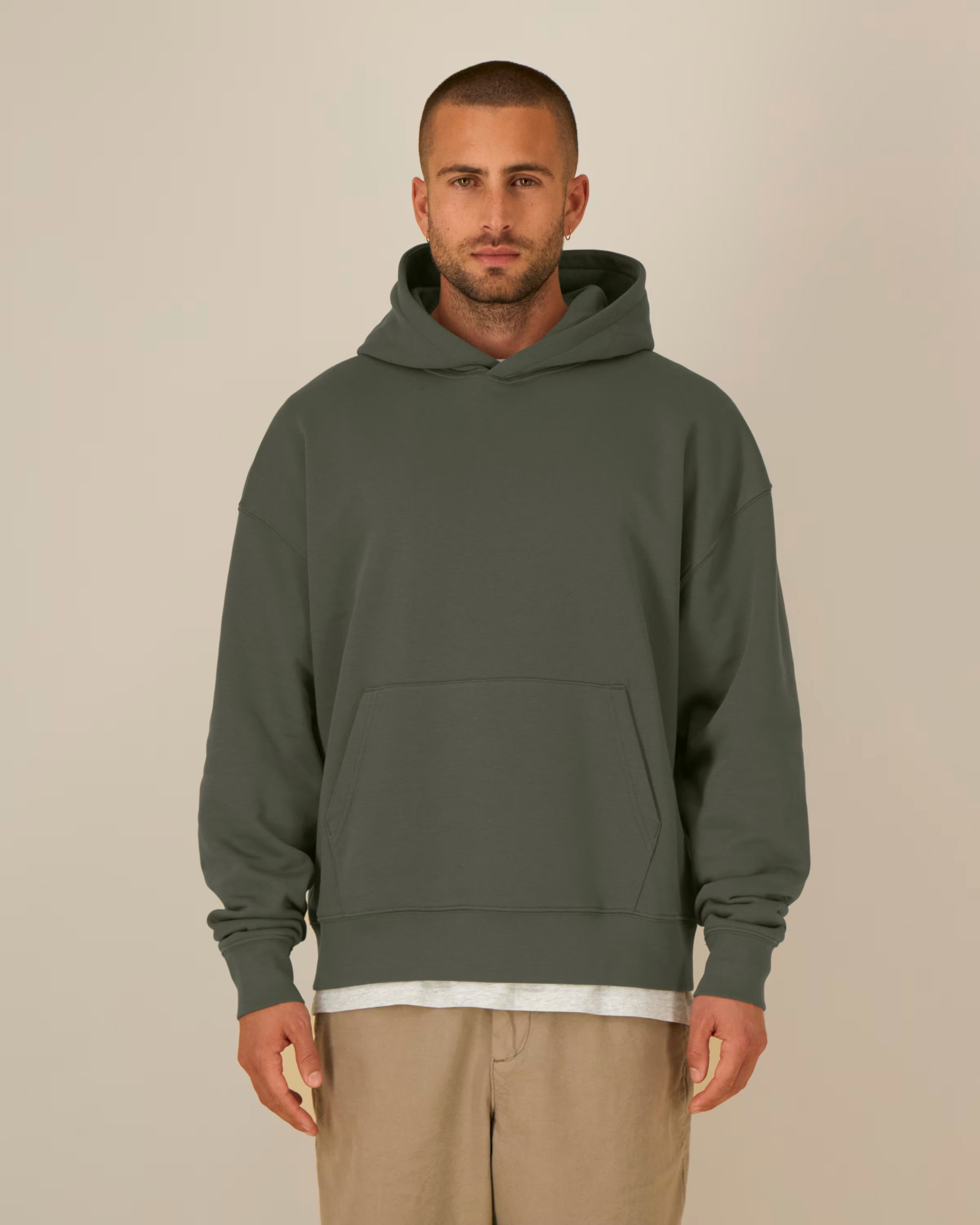 Man wearing a green unisex cotton hoodie and beige pants against a plain background