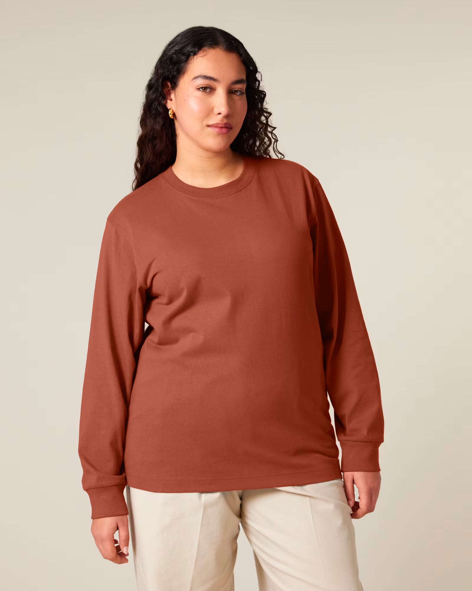 Front view of a female model wearing a rust orange cotton long sleeve t-shirt in studio
