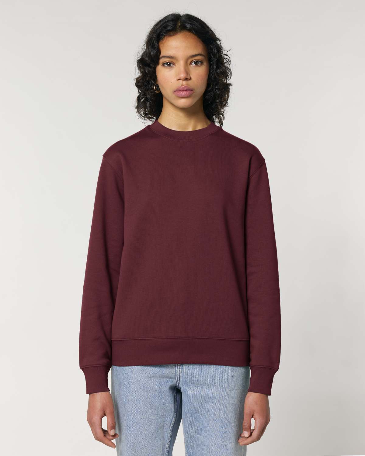 Person wearing a maroon unisex cotton sweatshirt and light blue jeans on a plain background