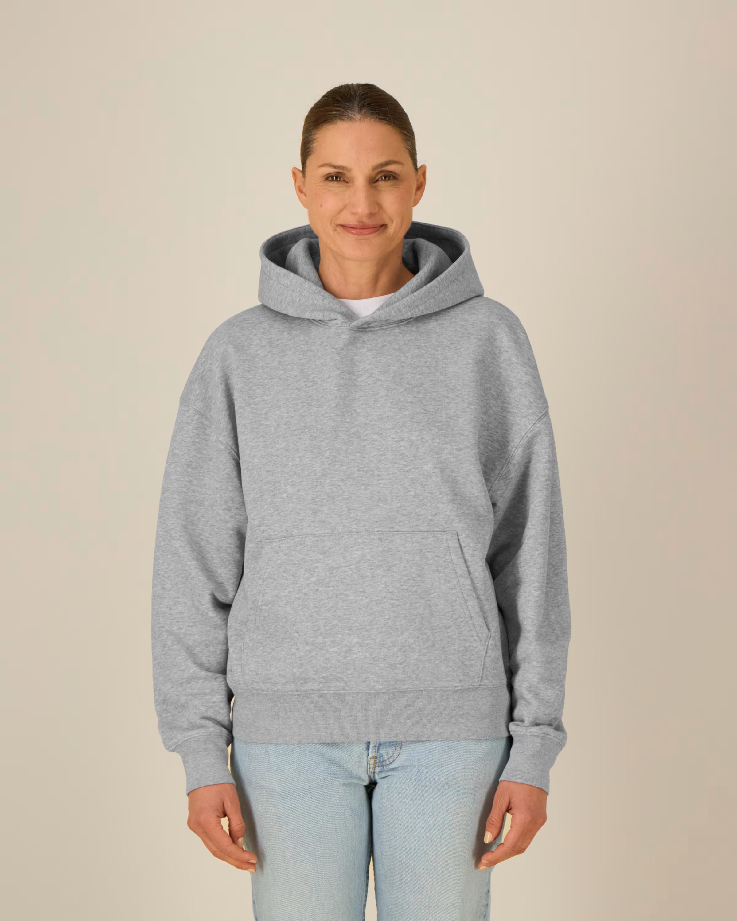 Woman wearing a gray unisex cotton hoodie and light blue jeans against a beige background