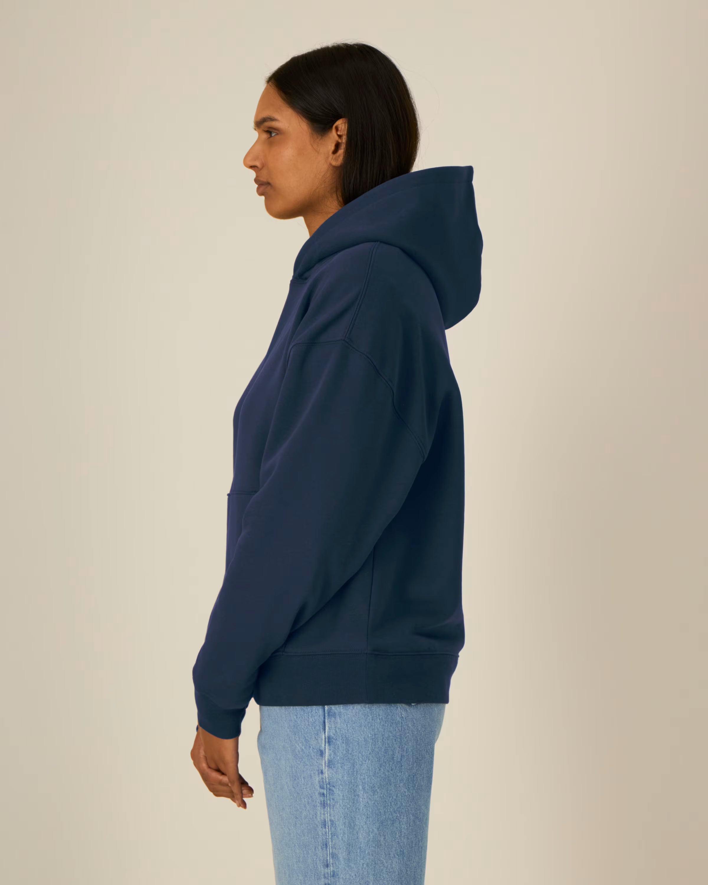 Person wearing a navy blue unisex cotton hoodie and light blue jeans on a beige background
