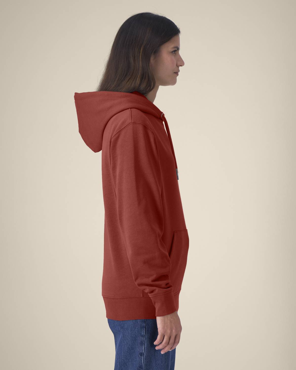 Person wearing a red hoodie and blue jeans on a beige background