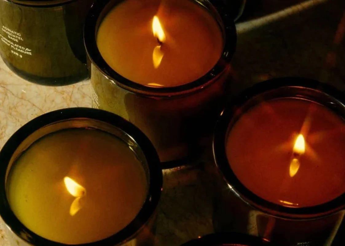 Three lit candles in black containers on a reflective surface.
