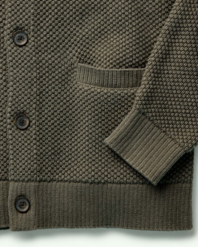 Close-up of a green knitted cardigan with buttons on a light gray background