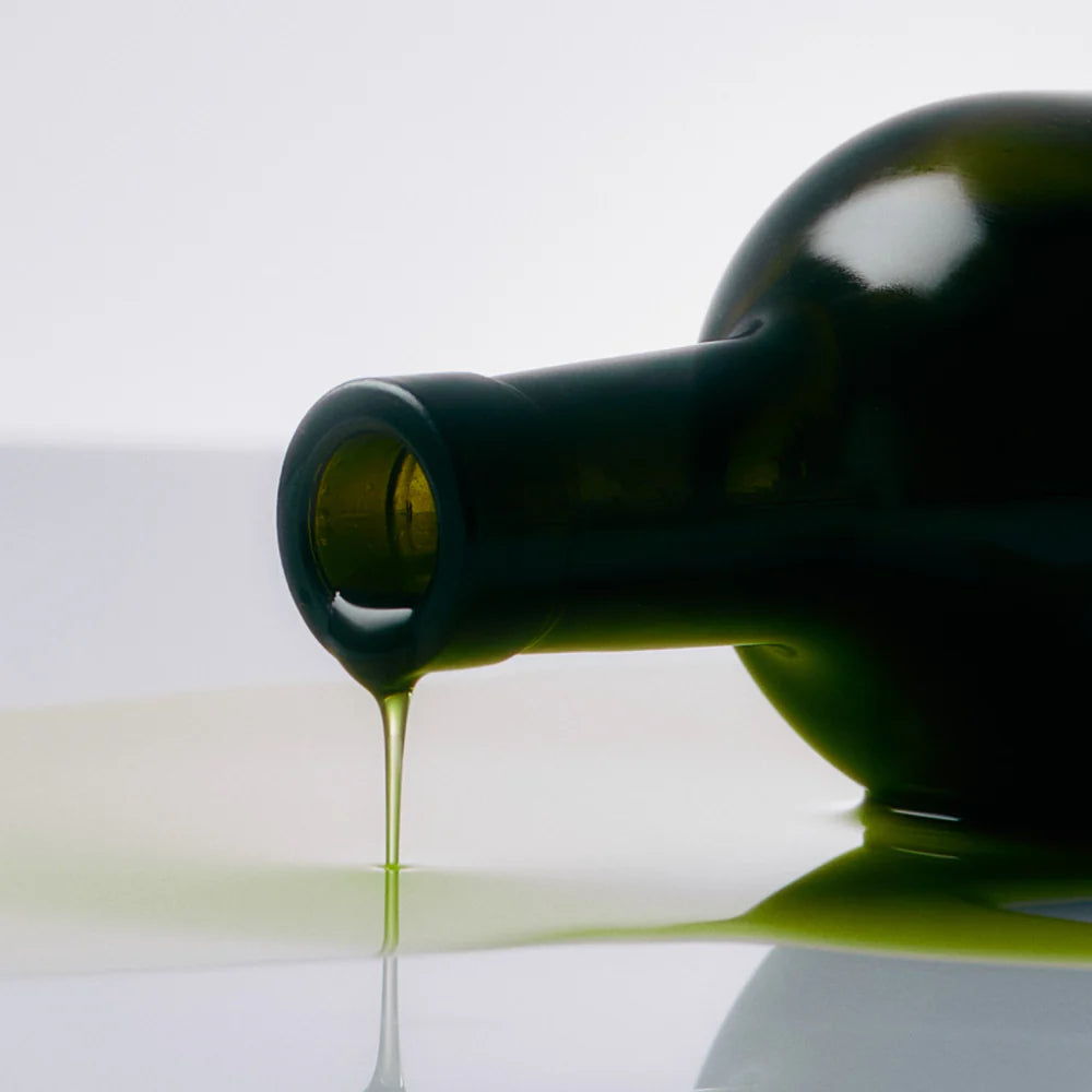 Green bottle pouring olive oil on a reflective surface with a white background