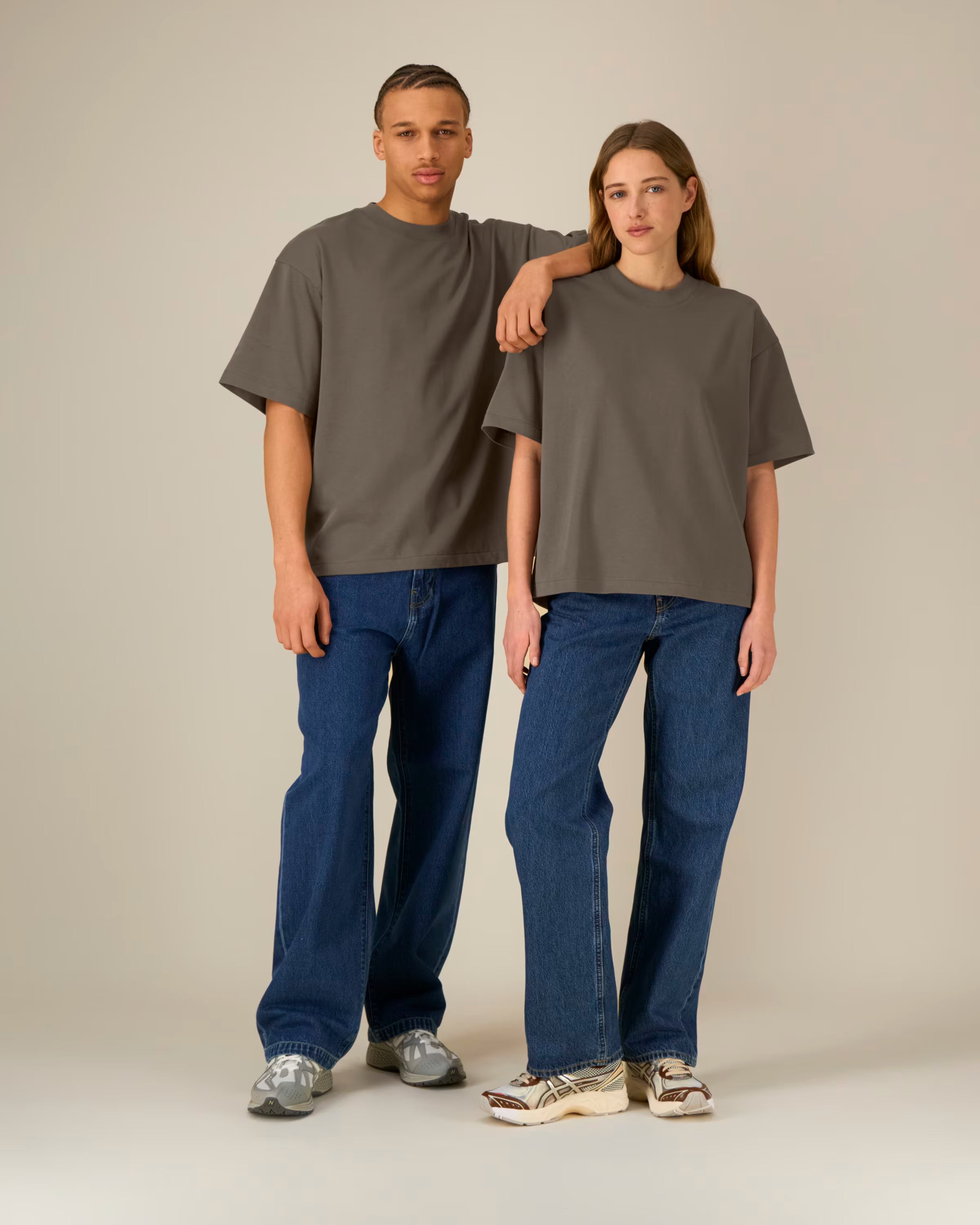 Two people wearing matching gray unisex cotton t-shirts and blue jeans standing against a plain background
