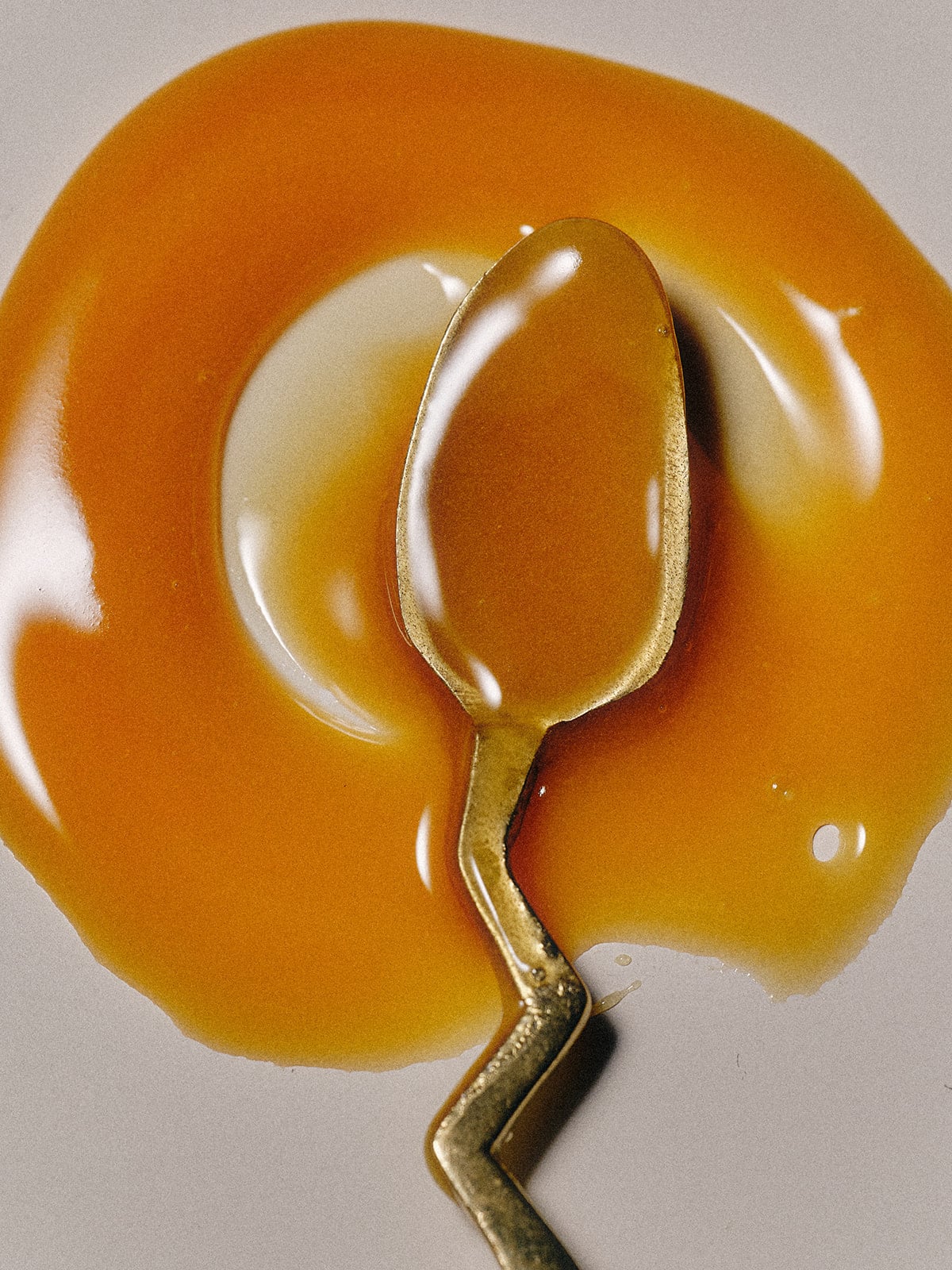 Gold spoon in a pool of caramel on a white background