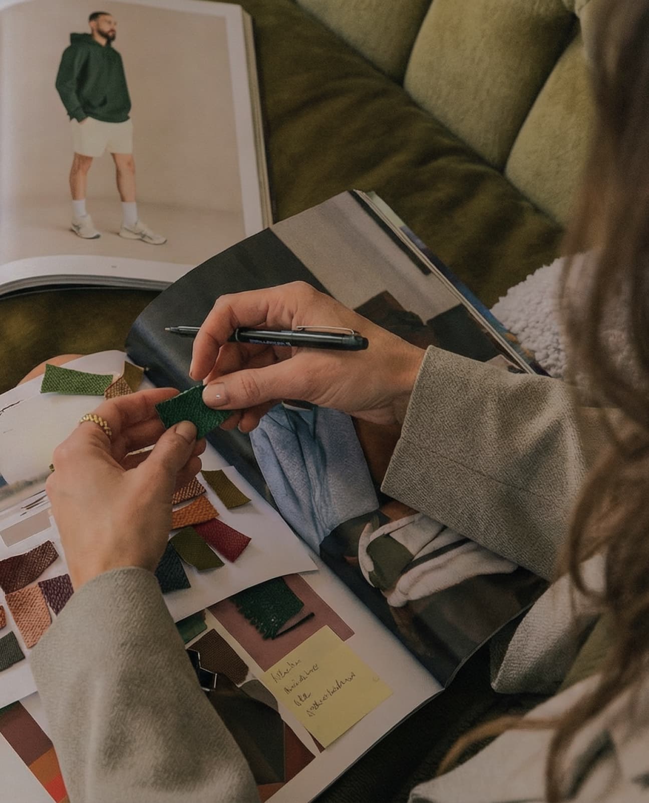 Person holding a pen and color swatches, with a magazine open on a couch in the background
