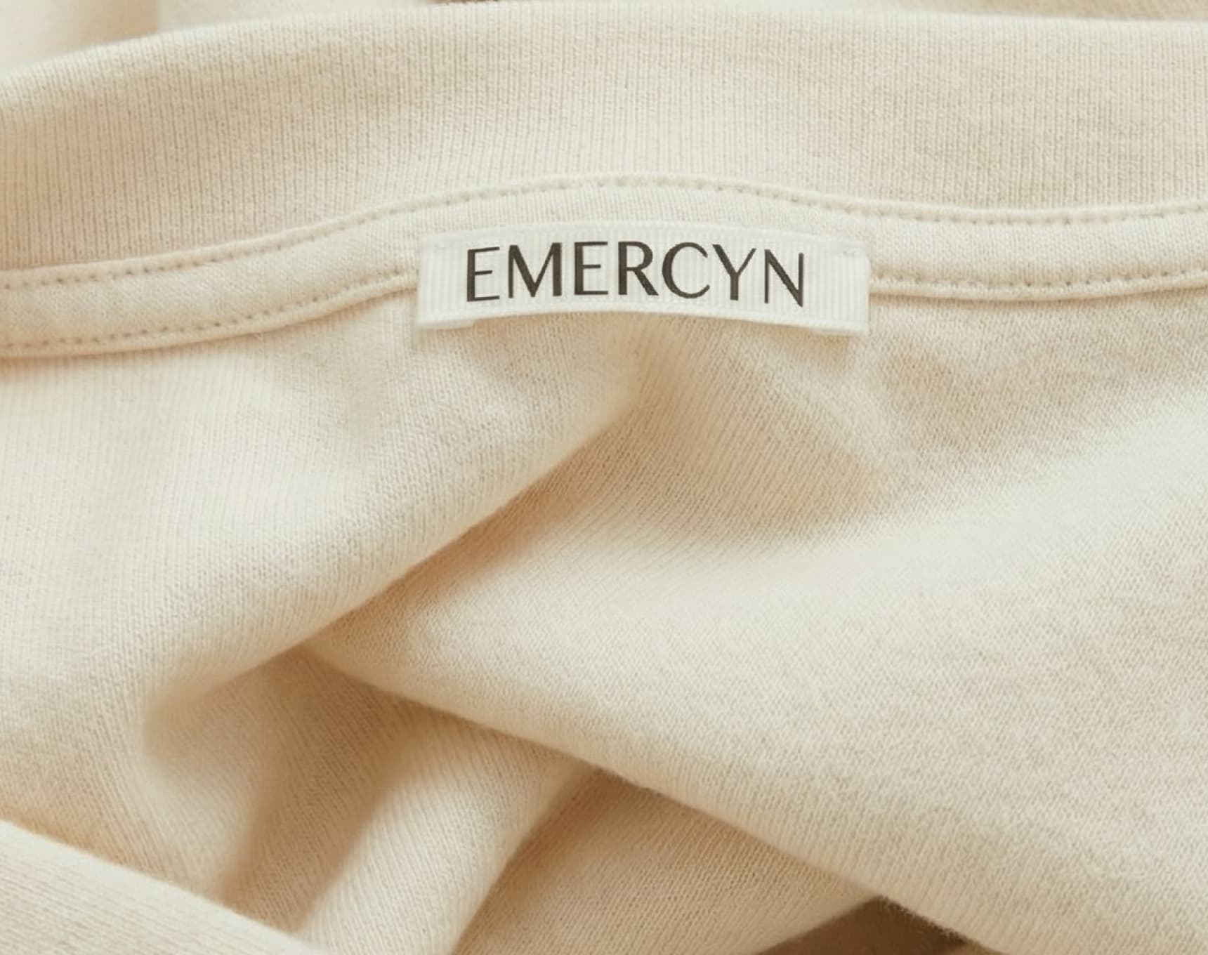 beige cotton fabric close-up with EMERCYN logo embroidery, sustainable premium textile detail