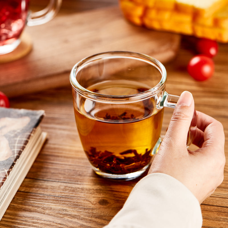 Woman holding clear borosilicate glass mug filled with tea