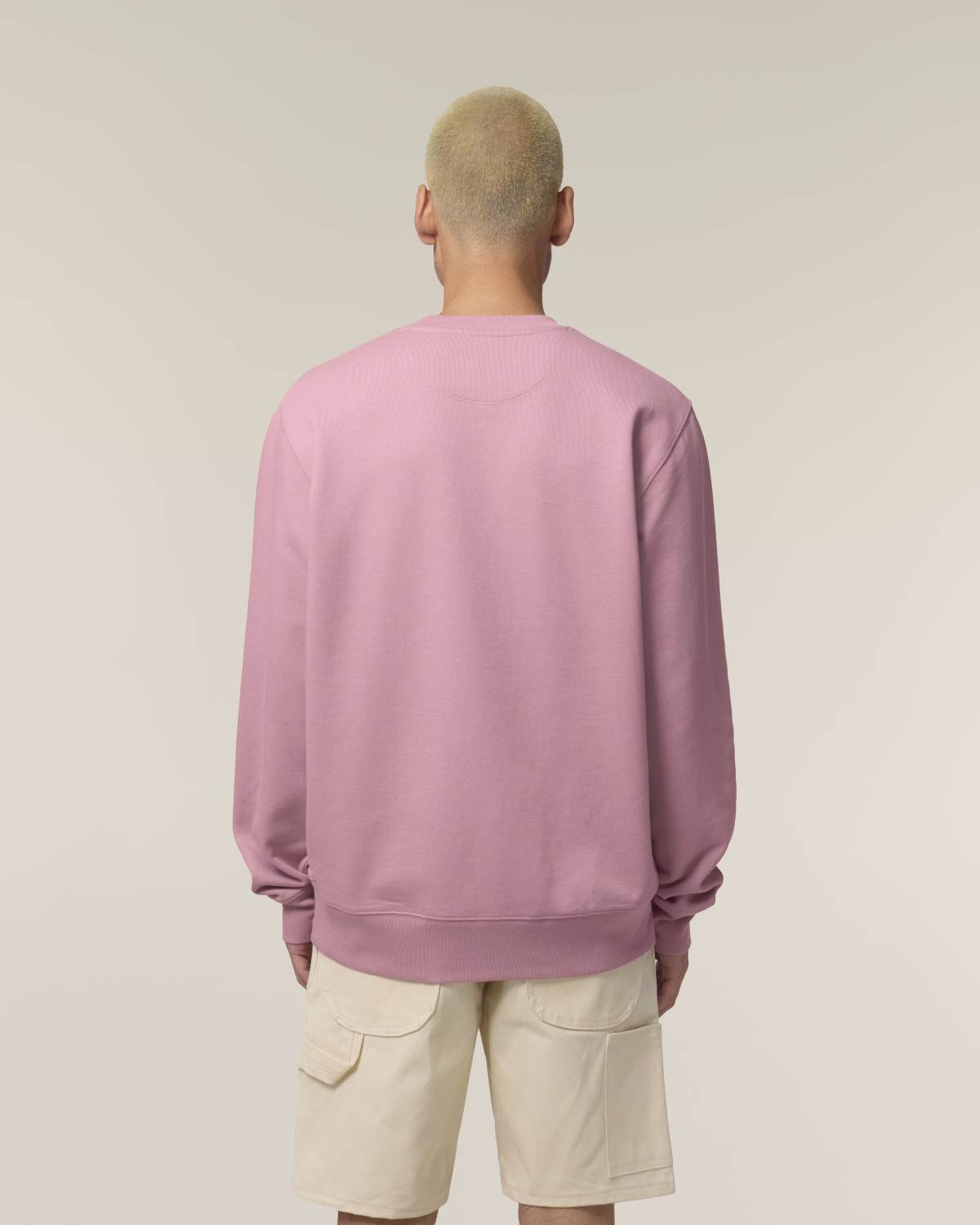 Person wearing a pink unisex cotton sweatshirt and beige shorts on a plain background