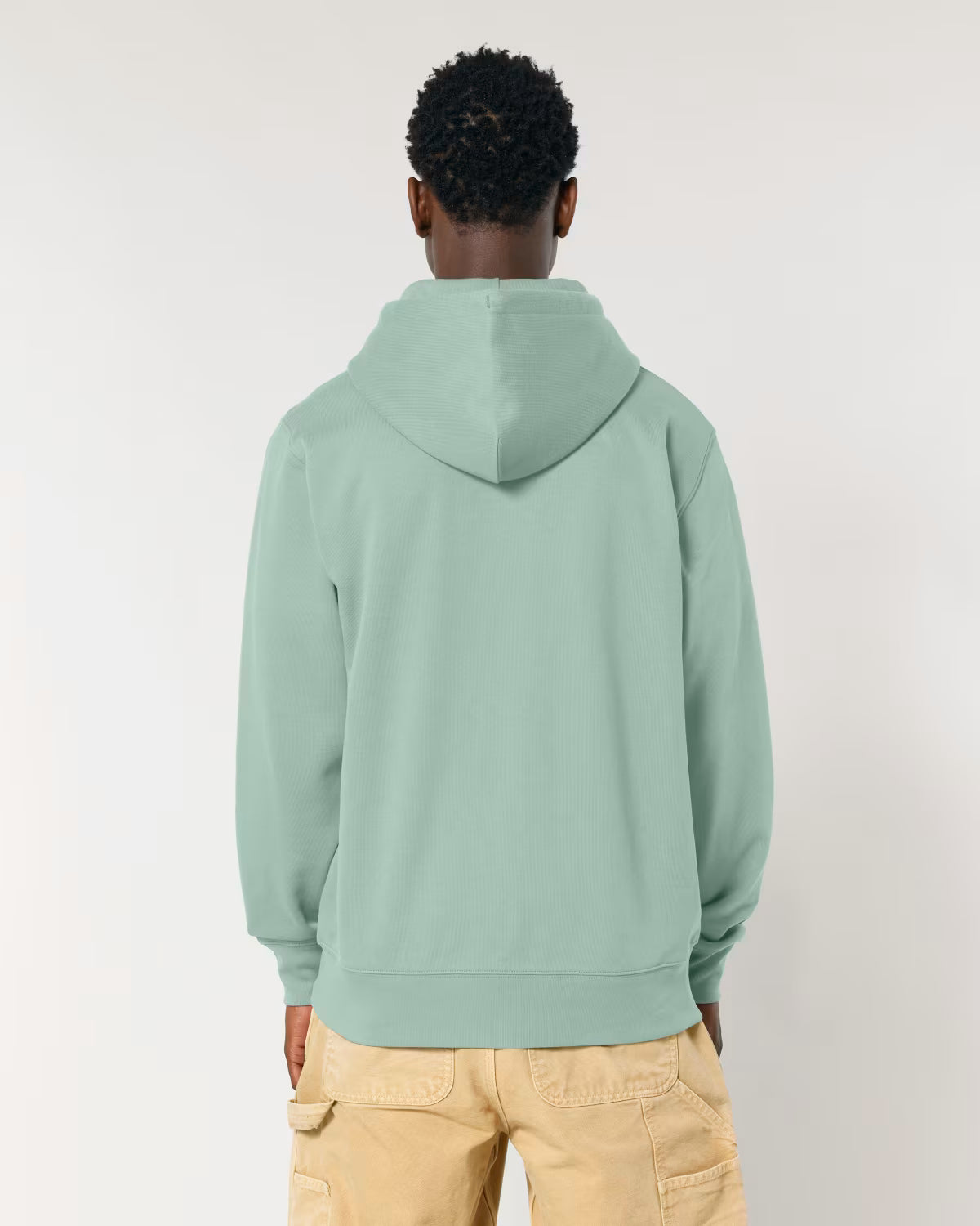 Person wearing a light green hoodie and beige pants on a plain background