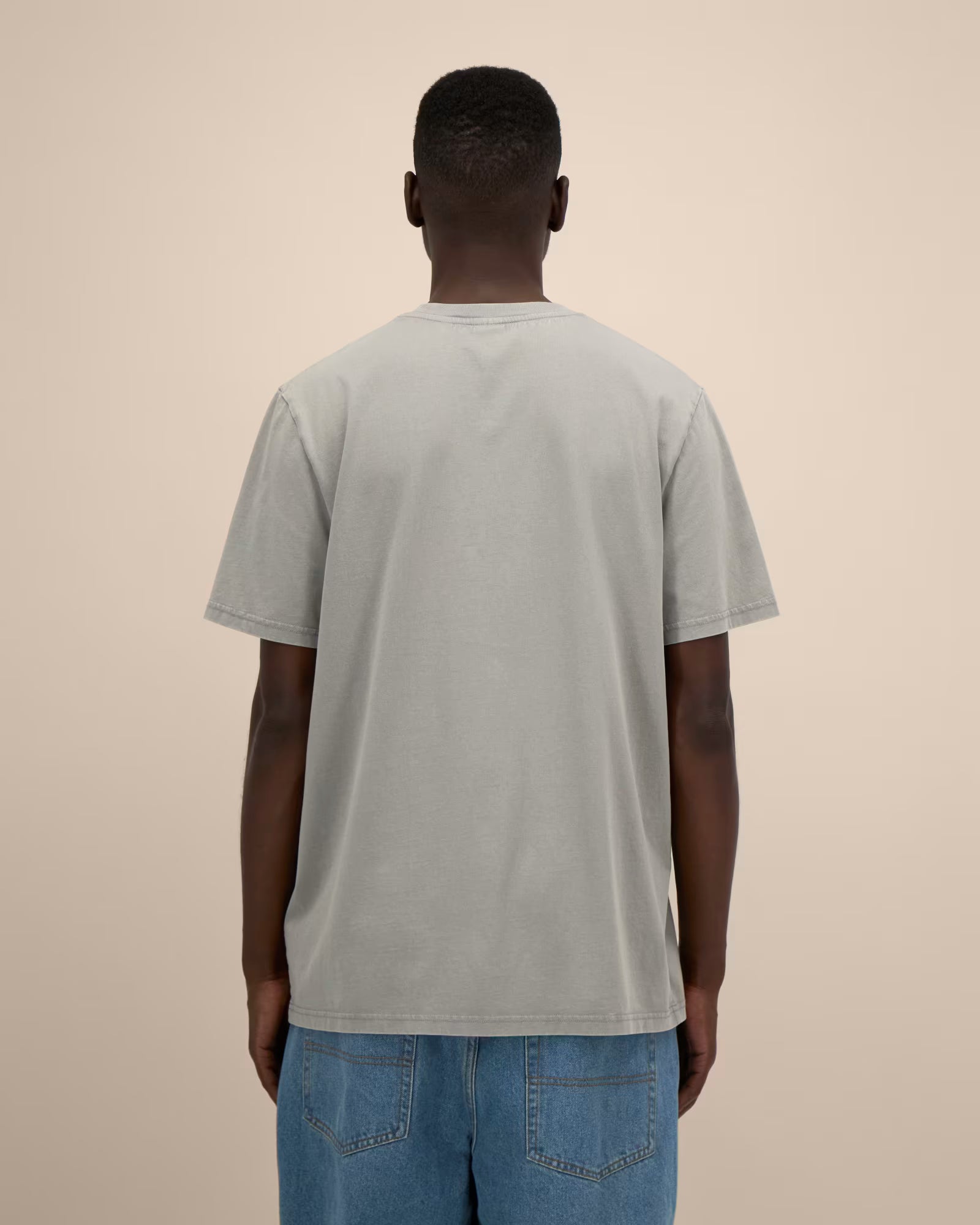 Back view of a man wearing a light grey cotton t-shirt in a studio setting