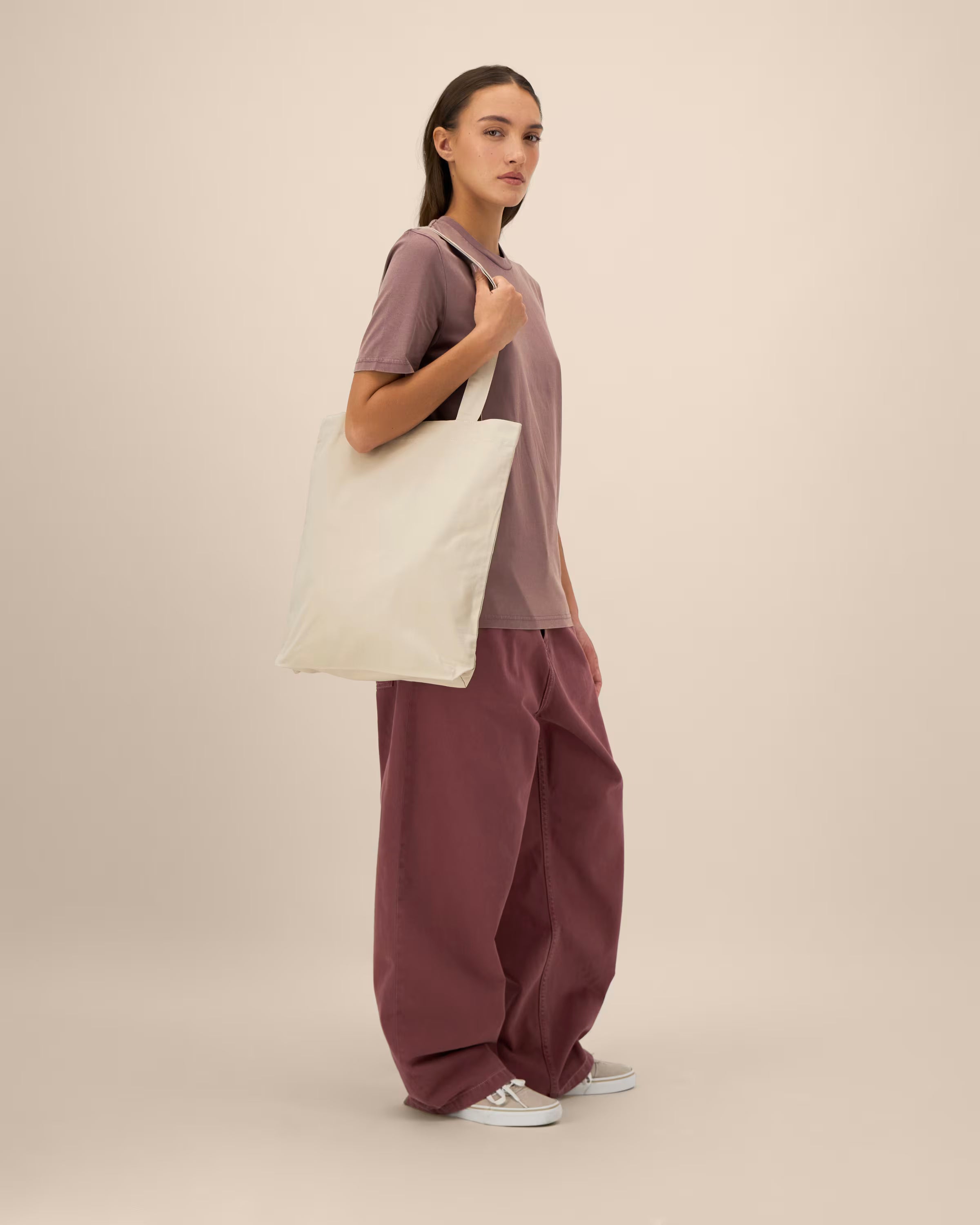 Woman holding a white tote bag against a beige background