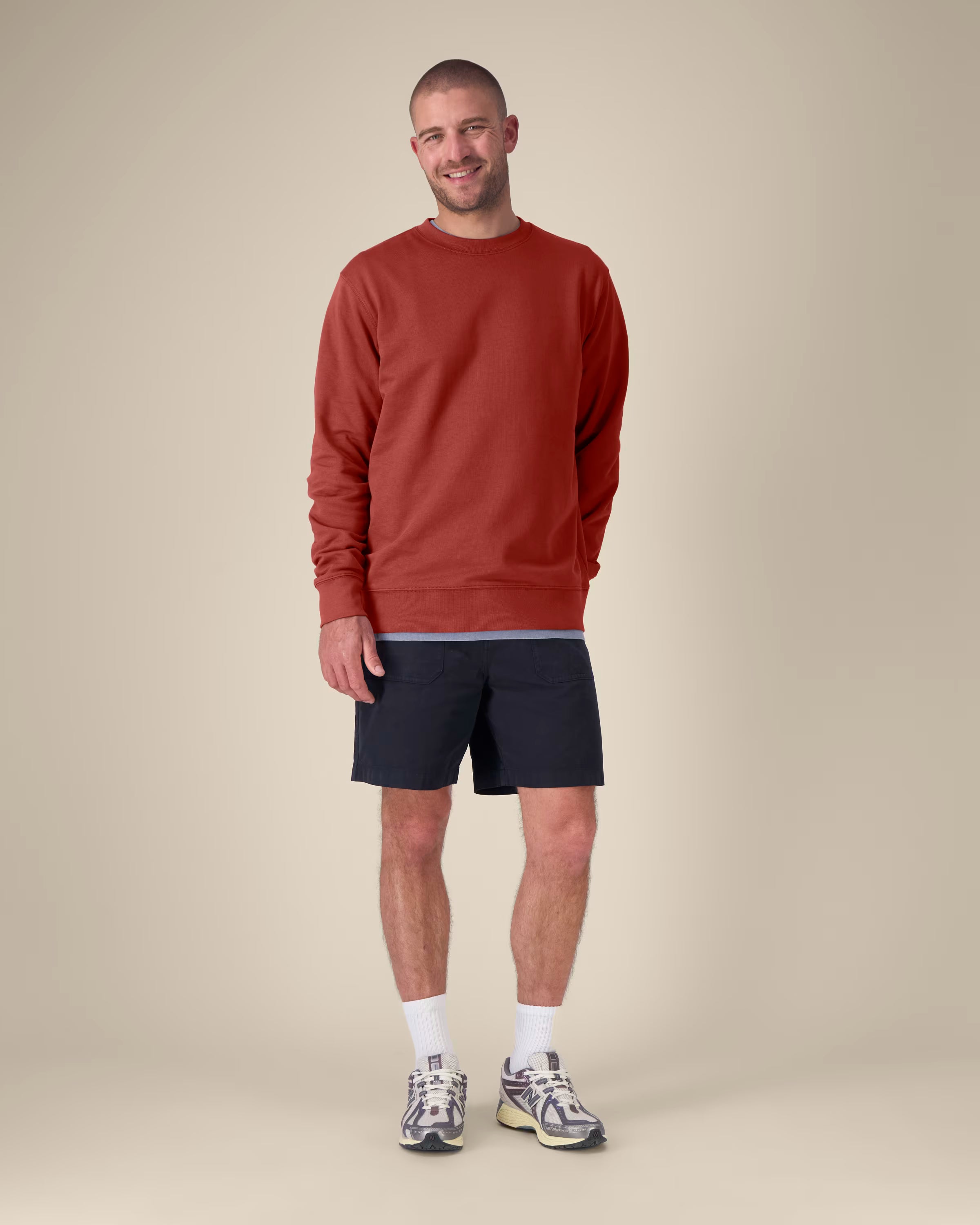 Man wearing a red unisex cotton sweatshirt and black shorts on a beige background