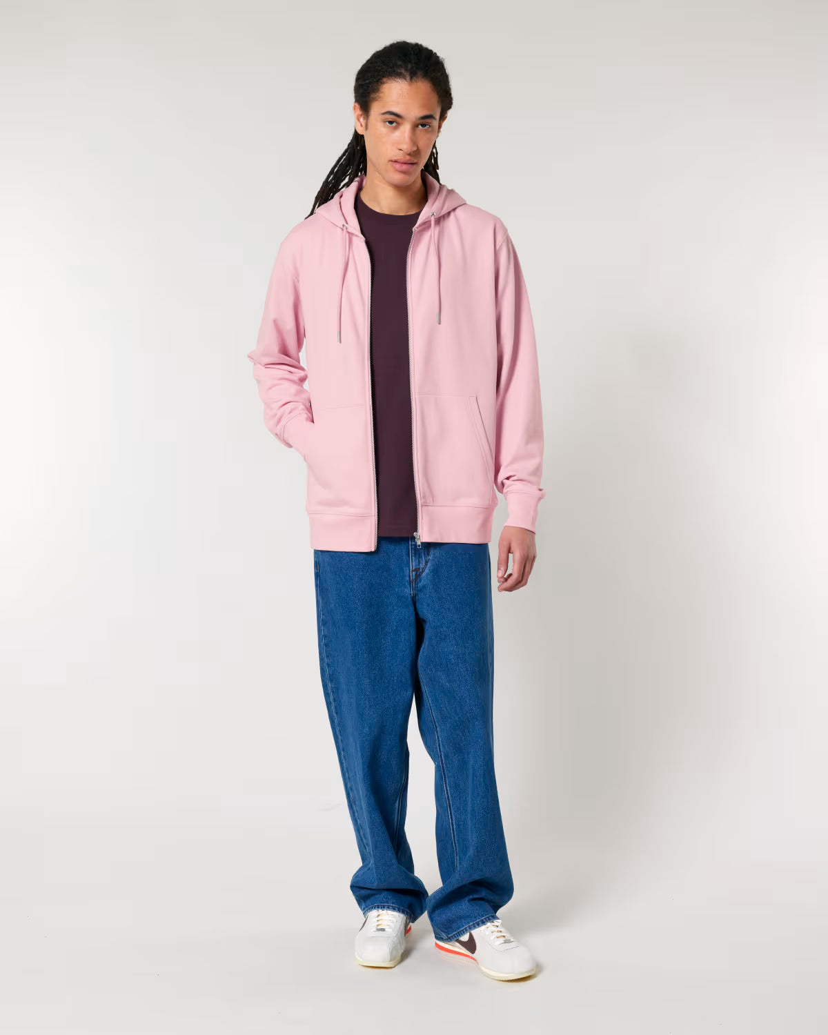 Person wearing a cotton pink hoodie, dark shirt, blue jeans, and white sneakers on a white background