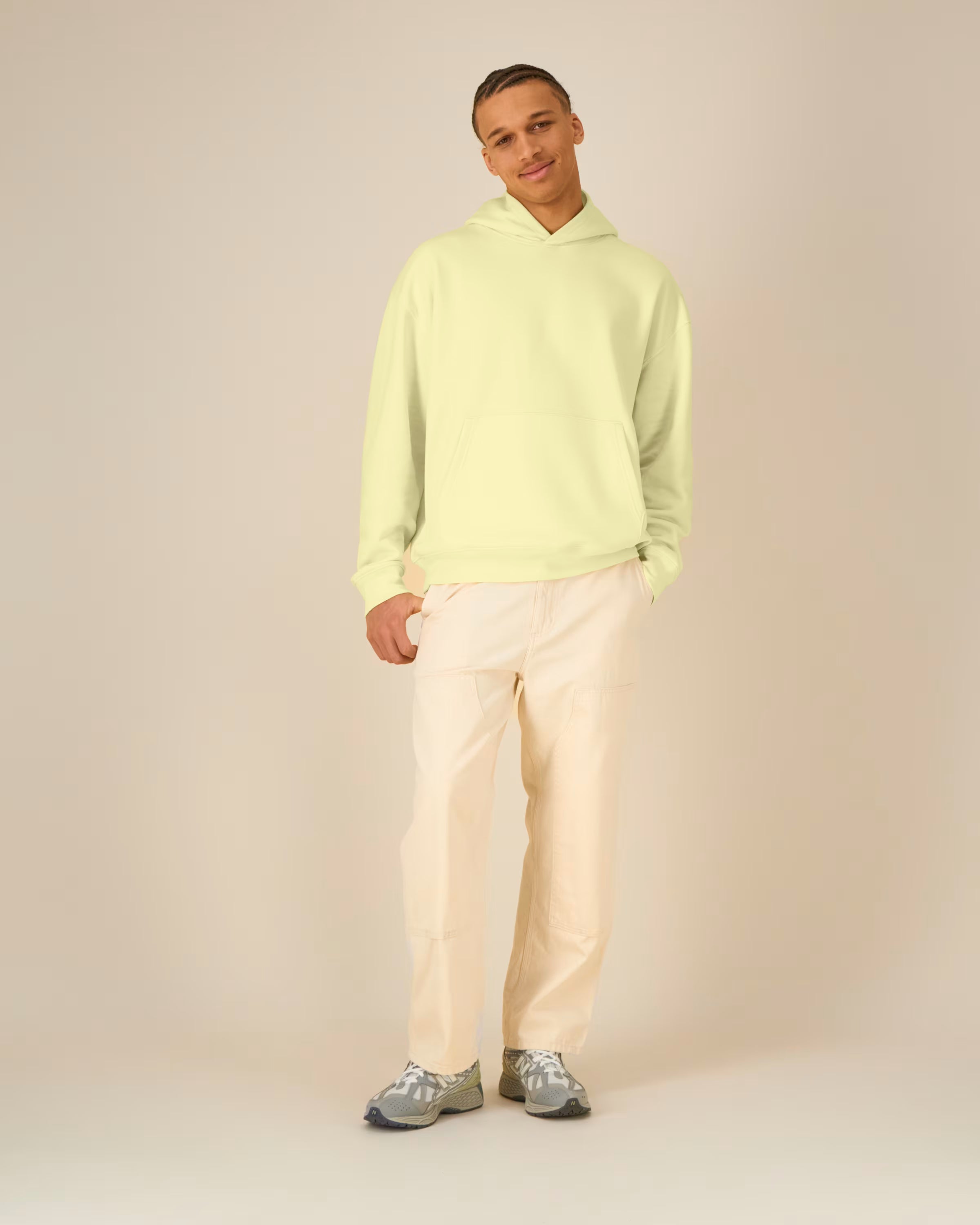 Man wearing a light green unisex cotton hoodie and beige pants on a plain background