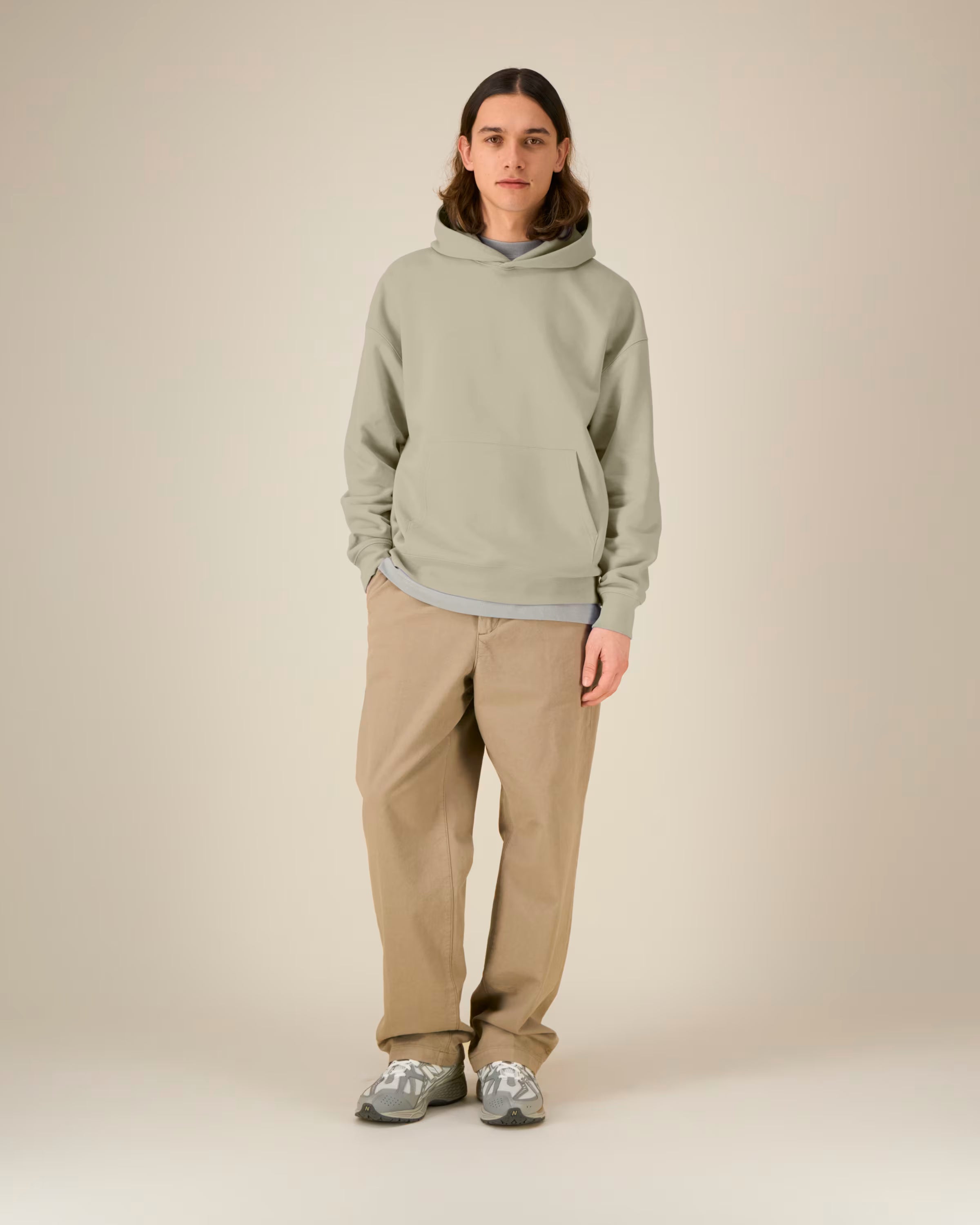 Person wearing a light green unisex cotton hoodie and beige pants on a plain background