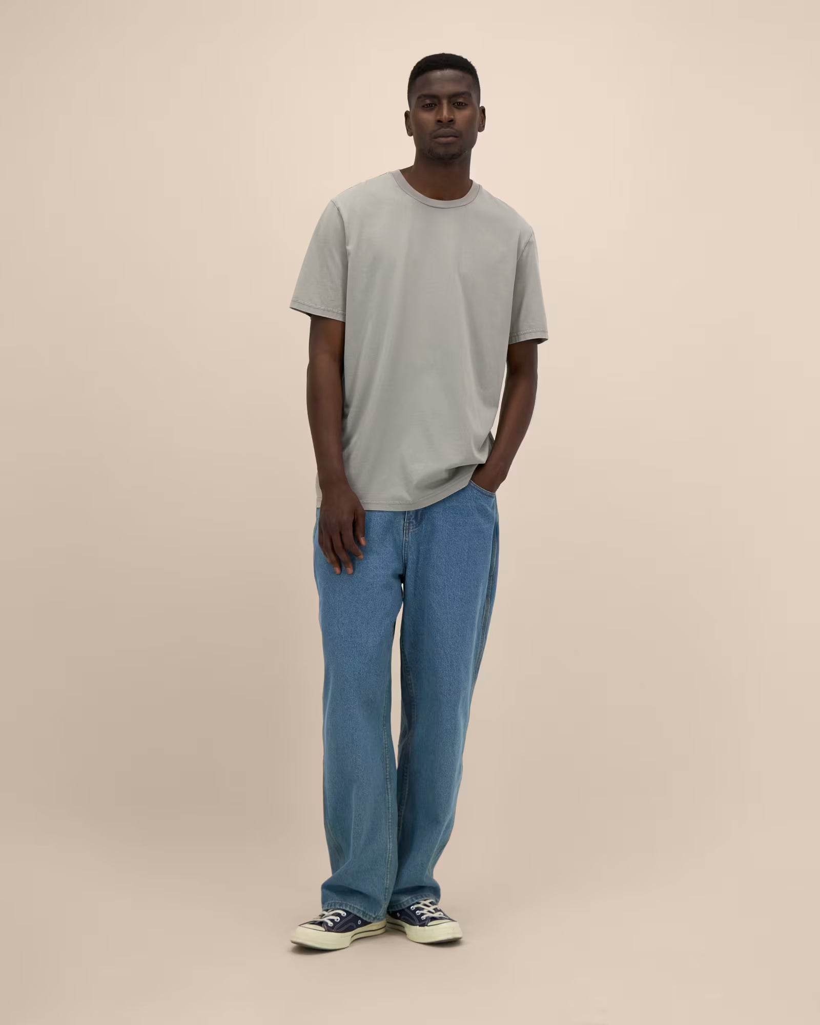 Full body front view of a man wearing a light grey t-shirt and jeans in studio