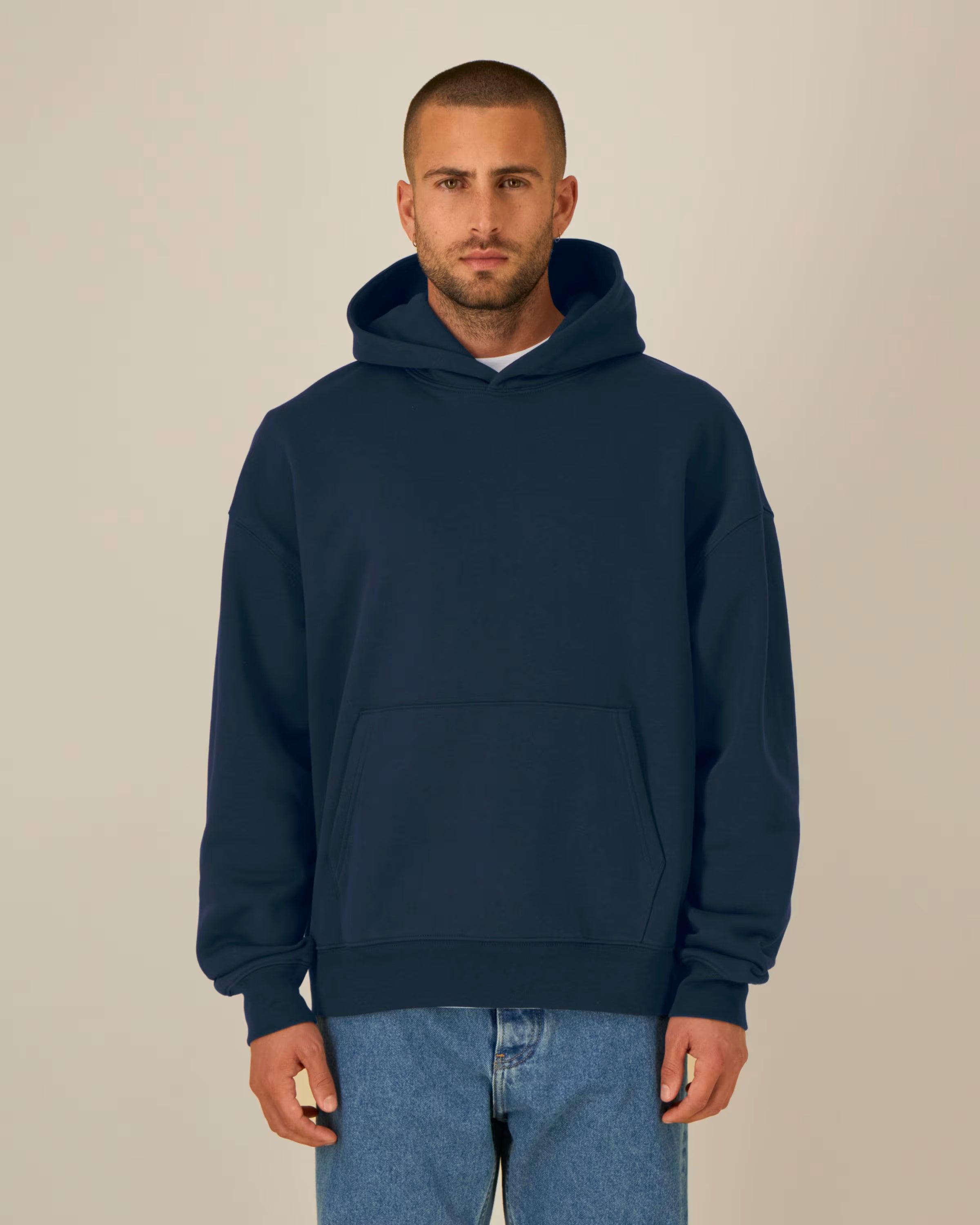 Man wearing a navy blue unisex cotton hoodie and blue jeans against a beige background