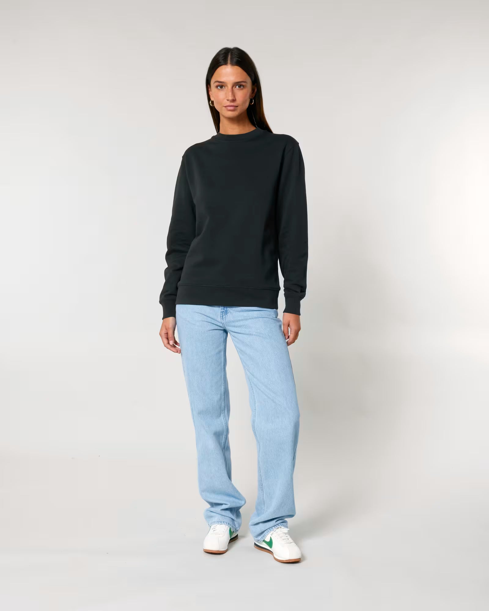 Person wearing a black unisex cotton sweater and light blue jeans on a plain background