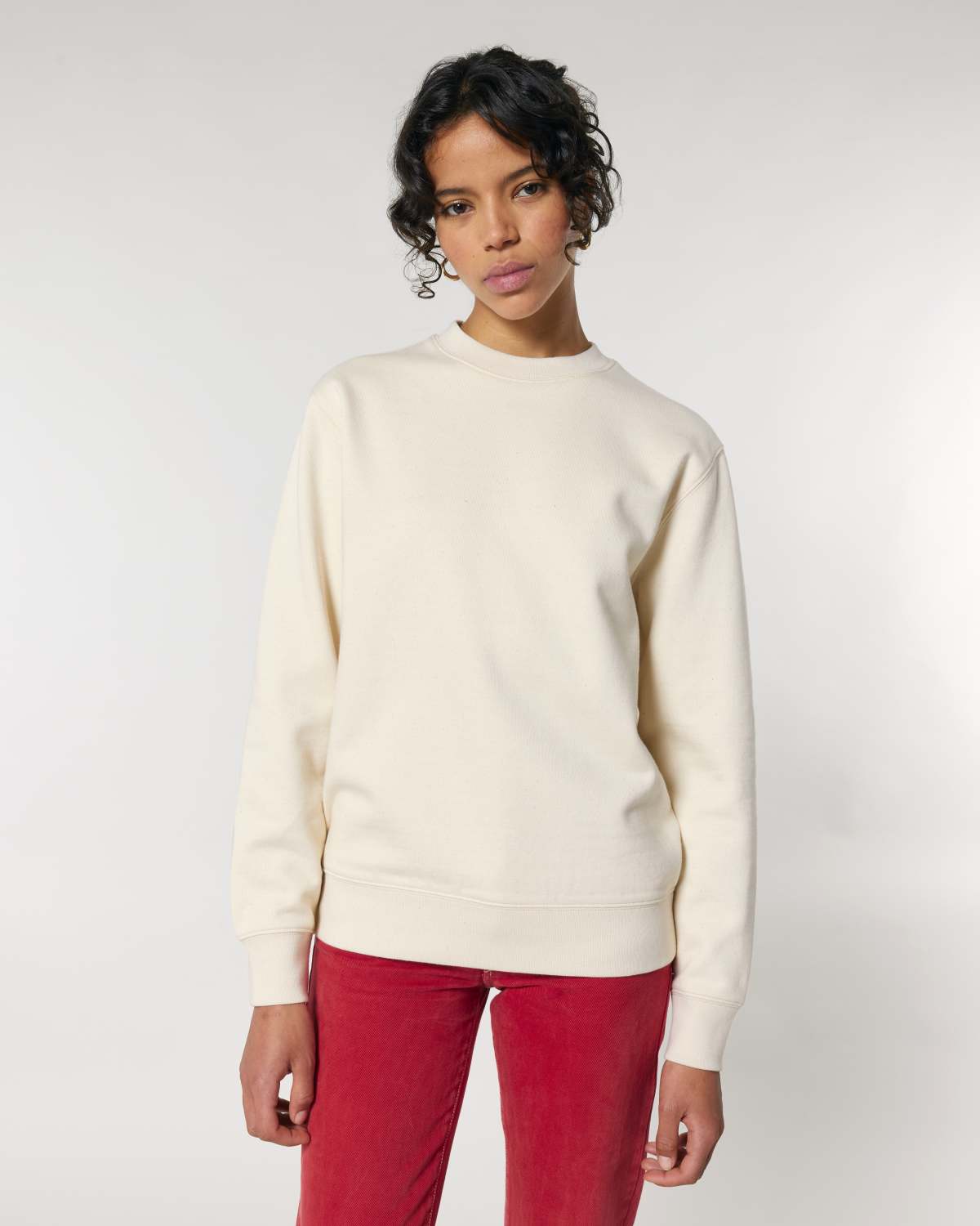 Person wearing a cream unisex cotton sweater and red pants on a white background