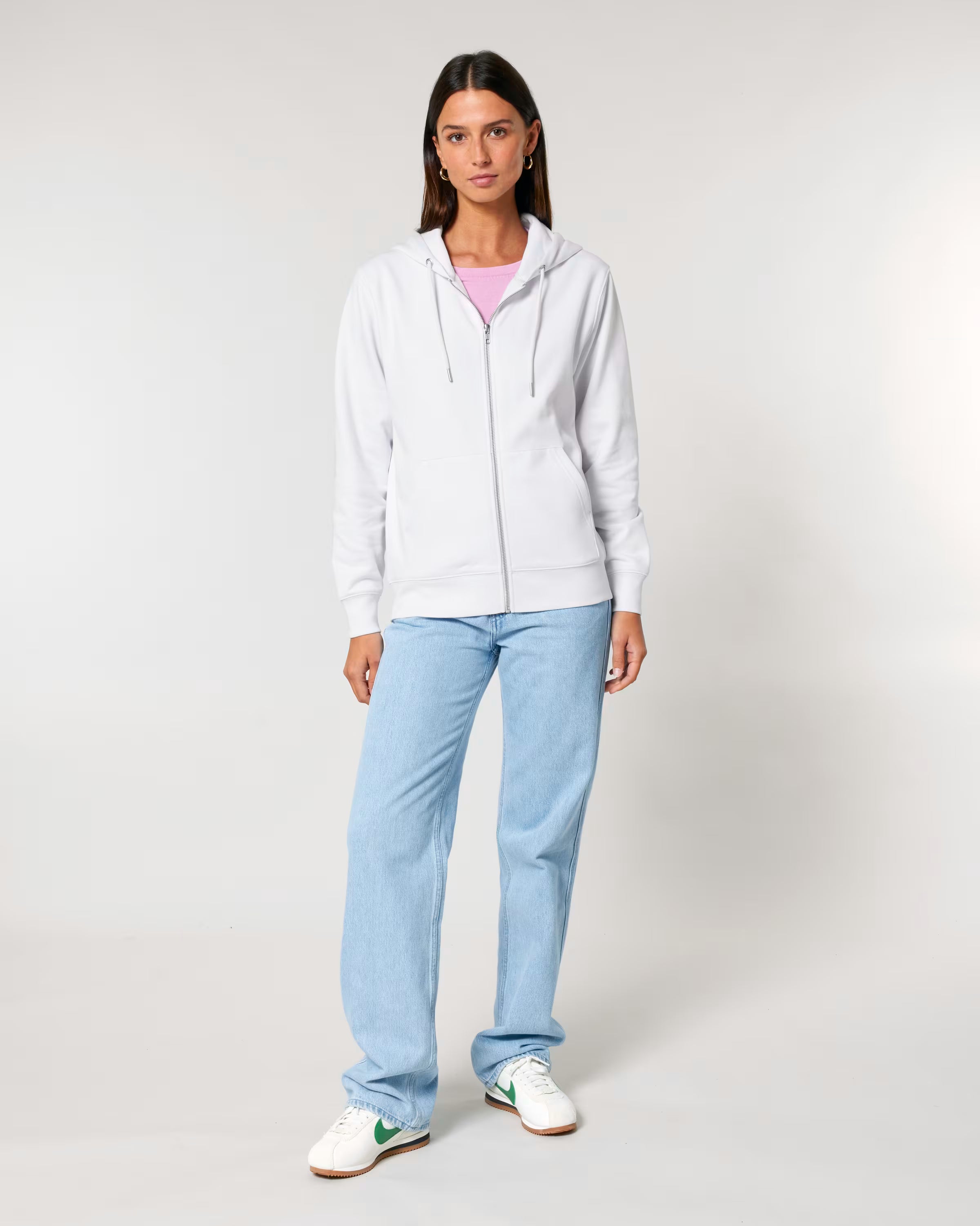 Woman wearing a white cotton hoodie, light blue jeans, and white sneakers on a plain background