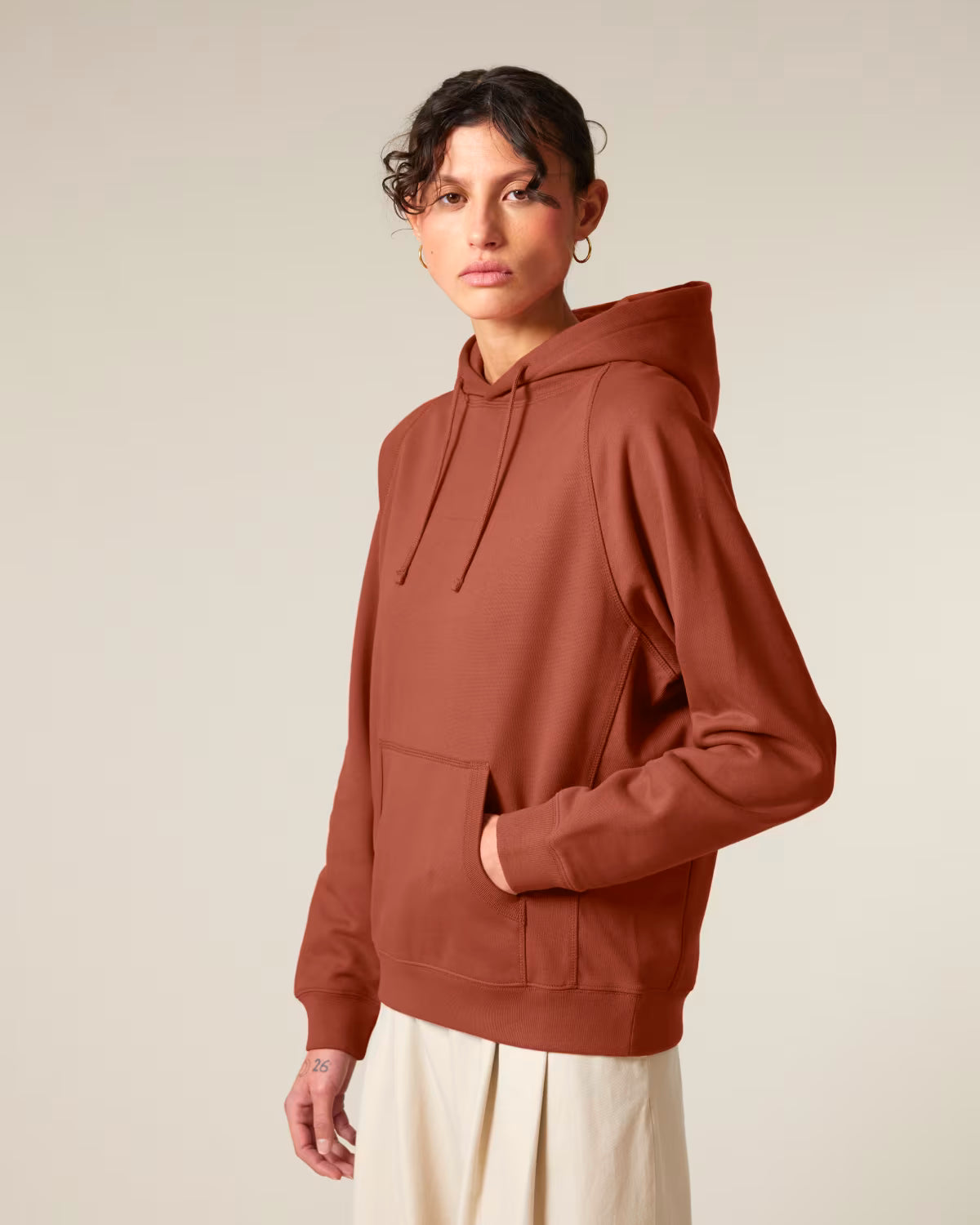 Front view of a female model wearing a rust orange cotton hoodie in studio