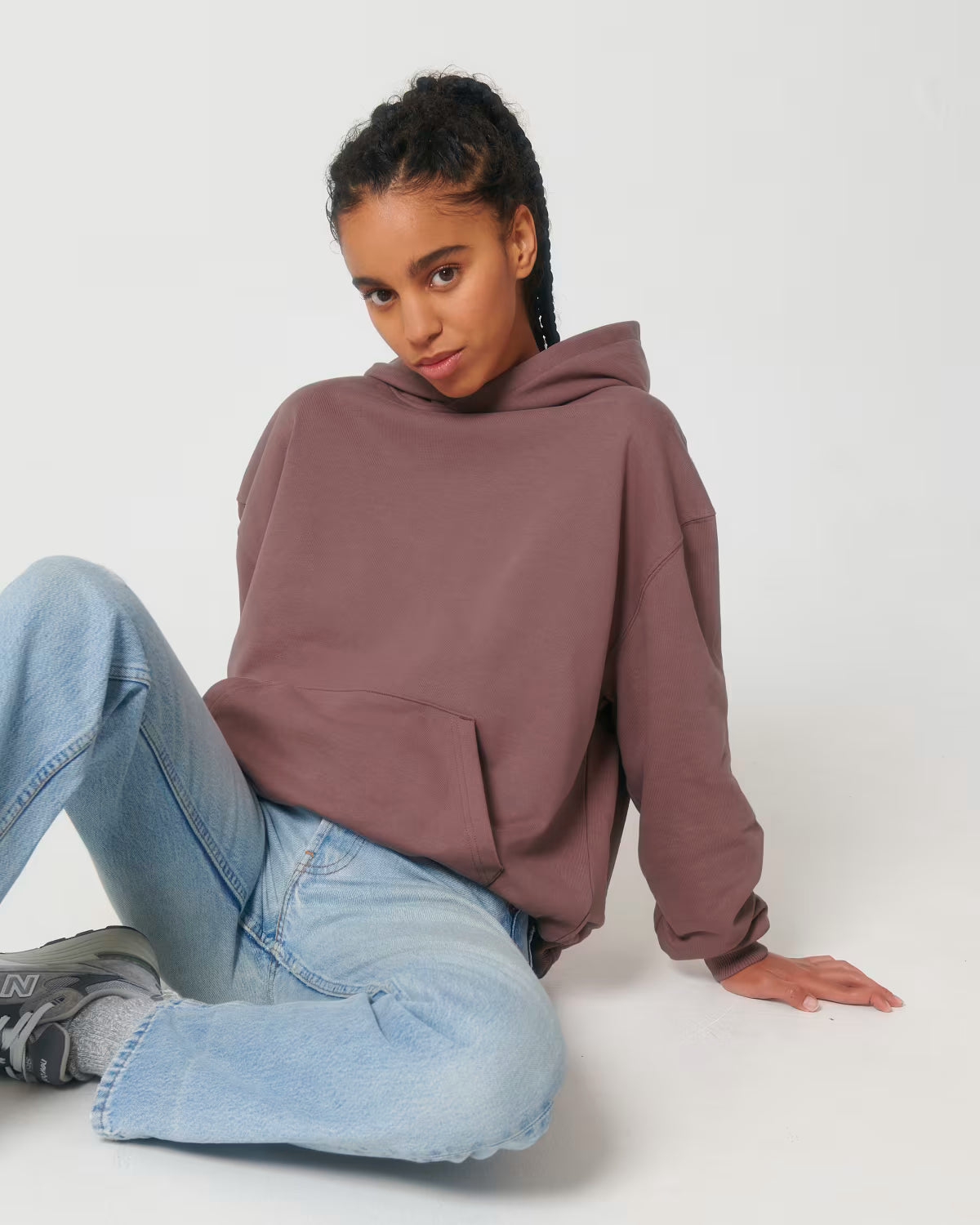 Lifestyle shot of a female model wearing a dusty rose cotton hoodie sitting in studio