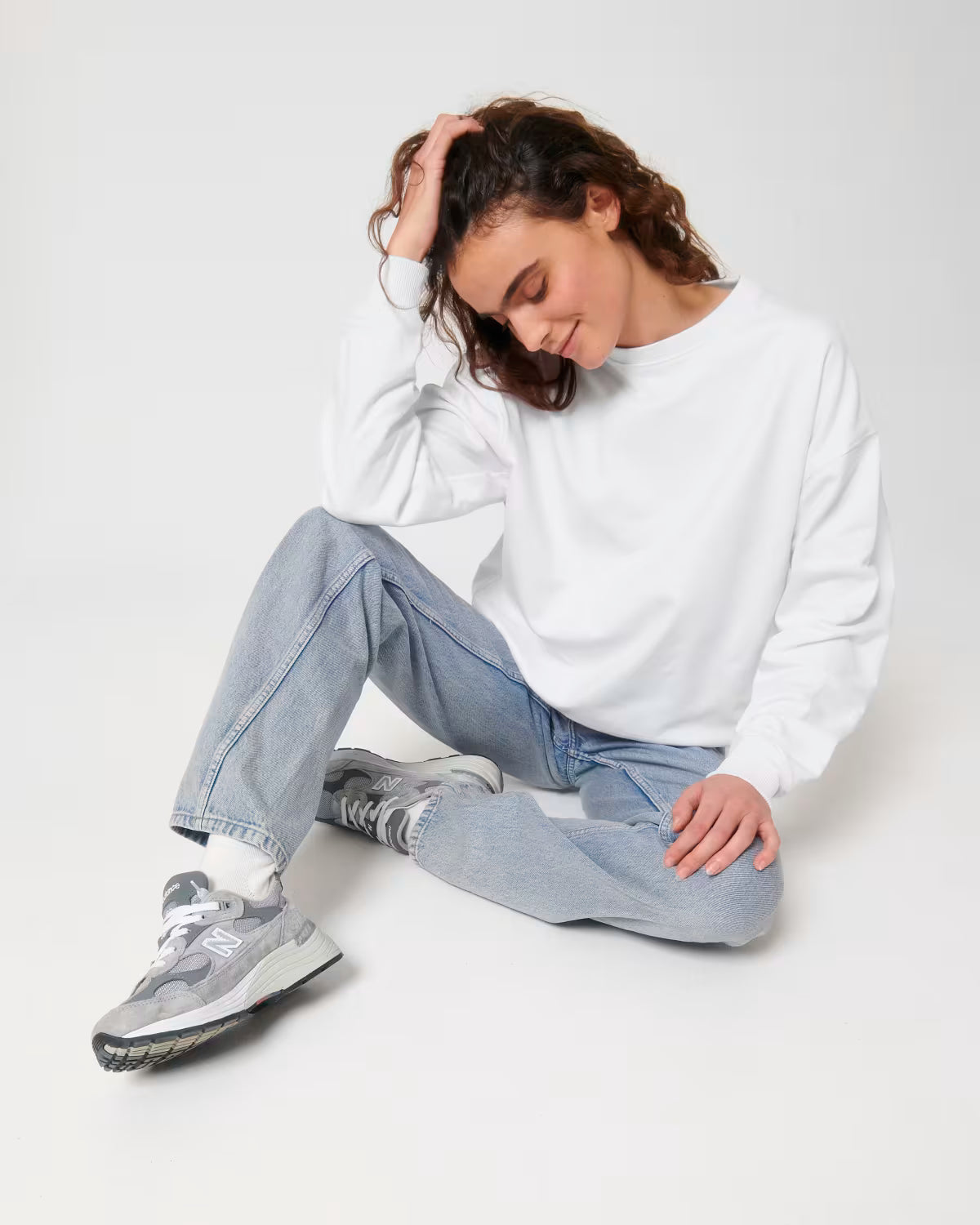Lifestyle shot of a female model wearing a white cotton hoodie sitting in studio