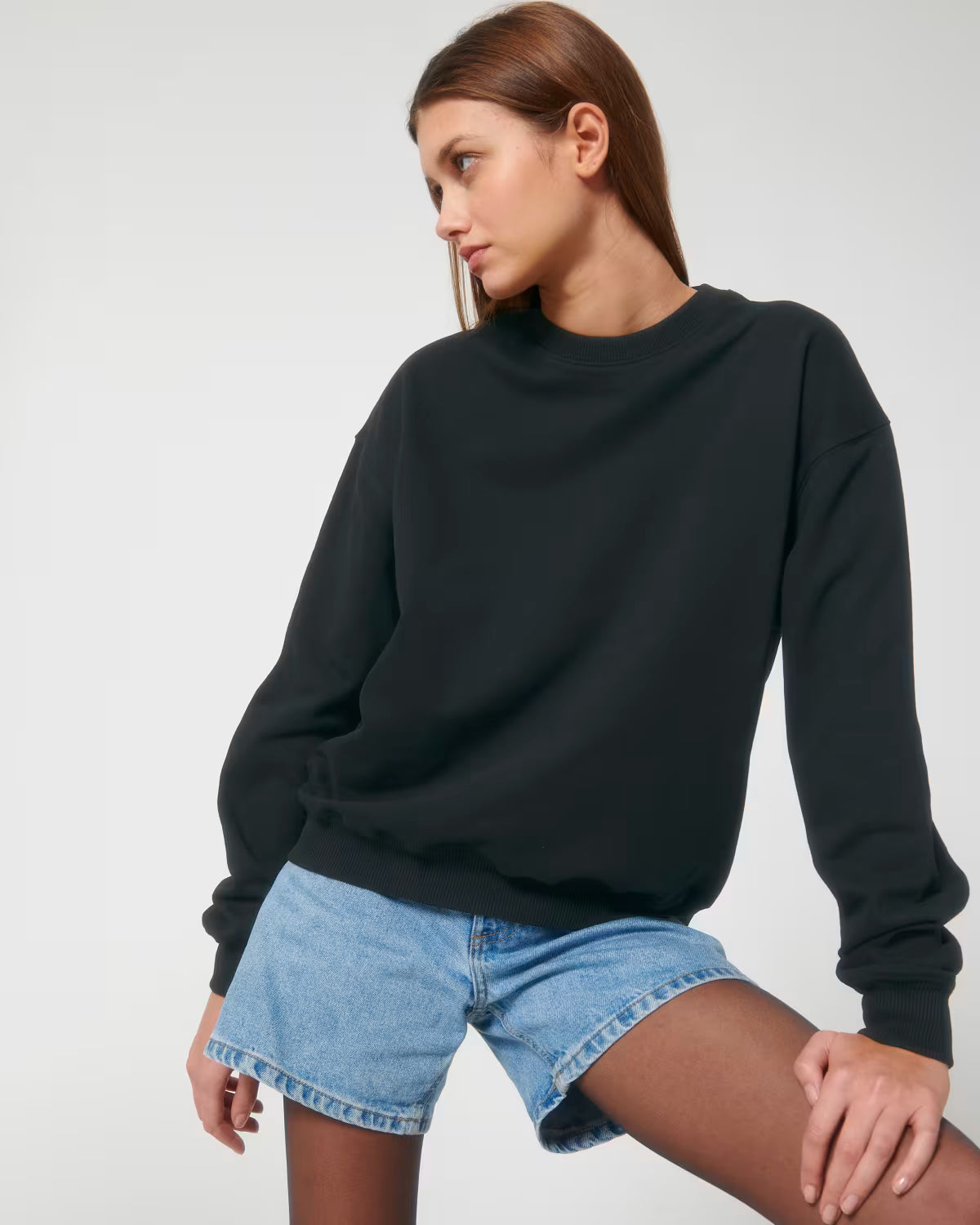 Lifestyle shot of a female model wearing a black cotton hoodie sitting in studio