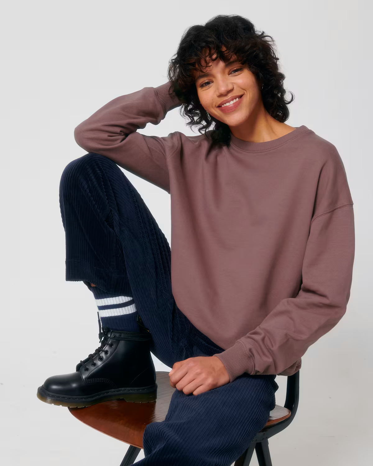 Lifestyle shot of a female model wearing a dusty rose cotton hoodie sitting in studio