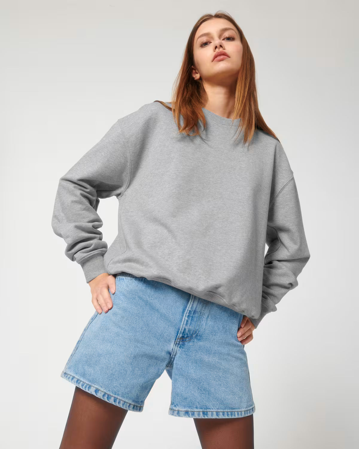 Lifestyle shot of a female model wearing a light grey cotton hoodie sitting in studio
