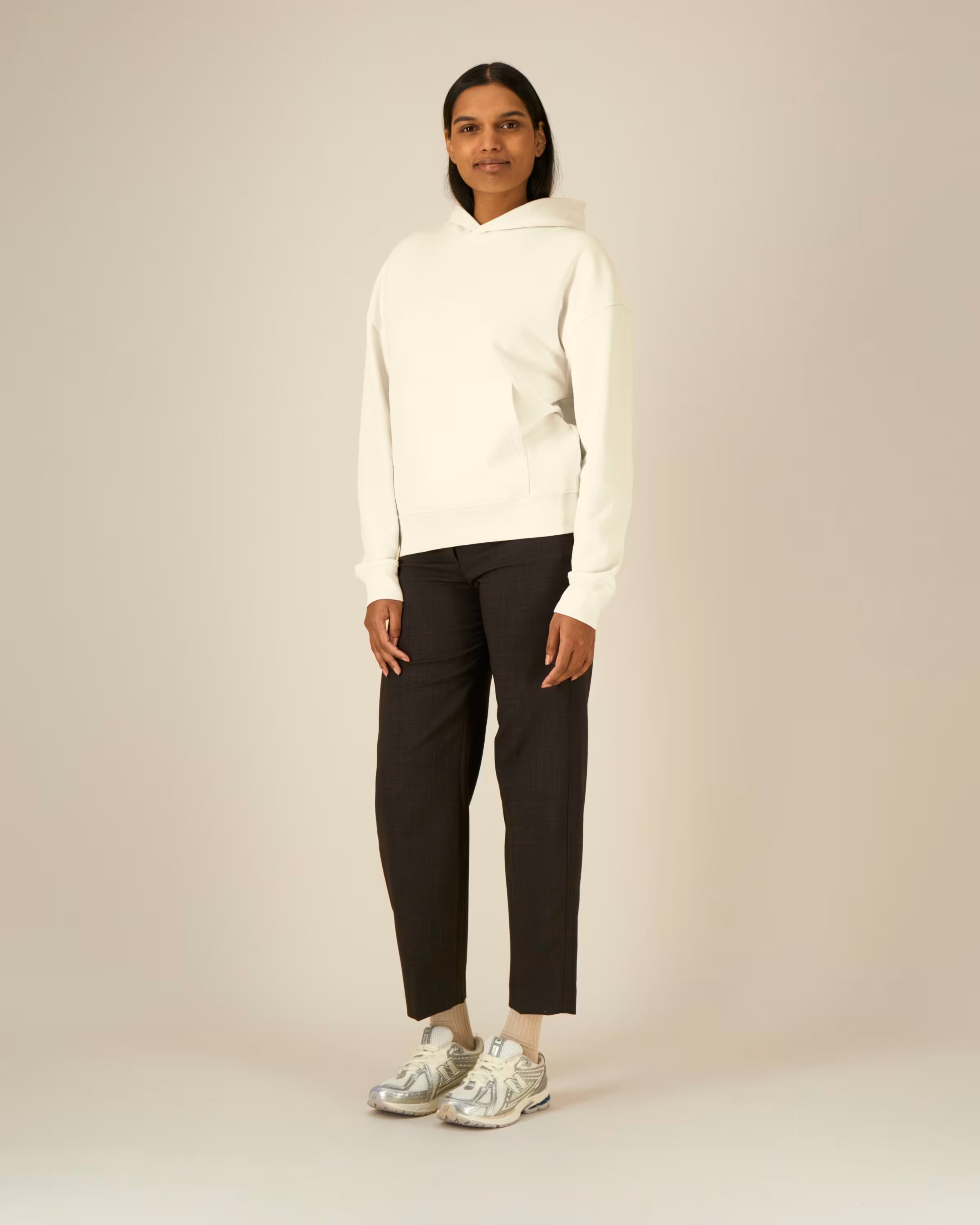 Person wearing a white unisex cotton hoodie and black pants on a plain background