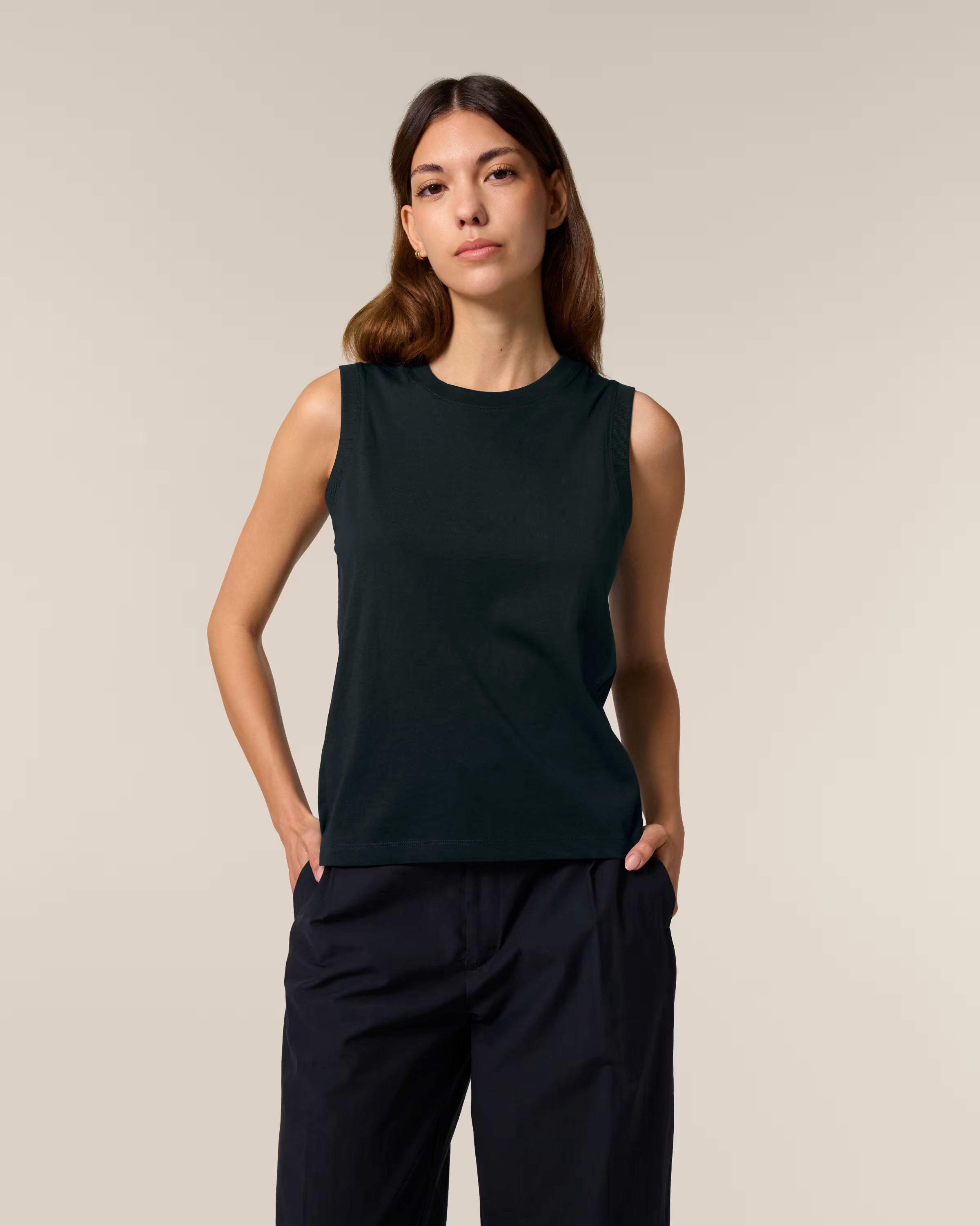 Woman wearing a black unisex cotton sleeveless top and pants against a beige background