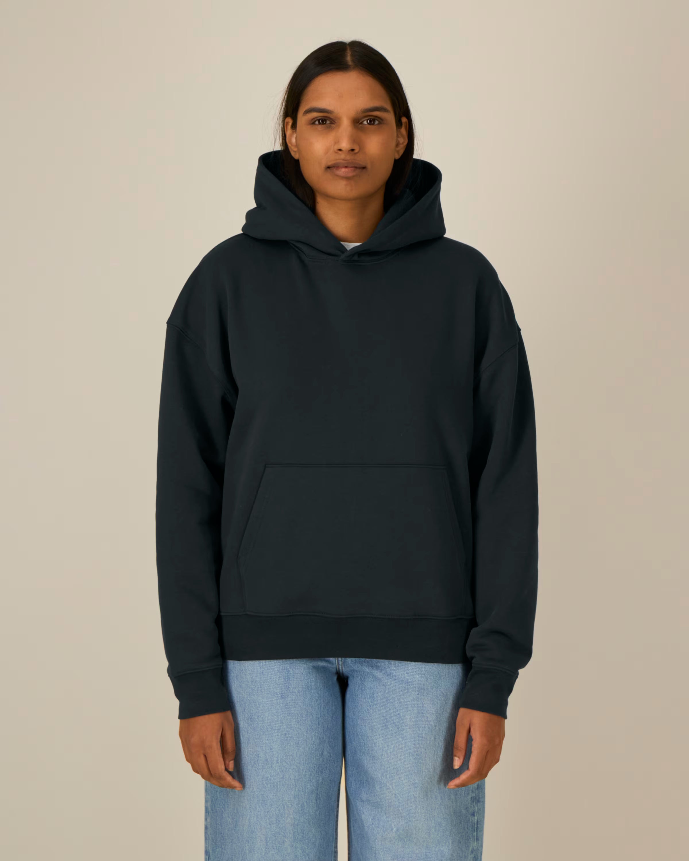 Person wearing a black unisex cotton hoodie and light blue jeans on a beige background