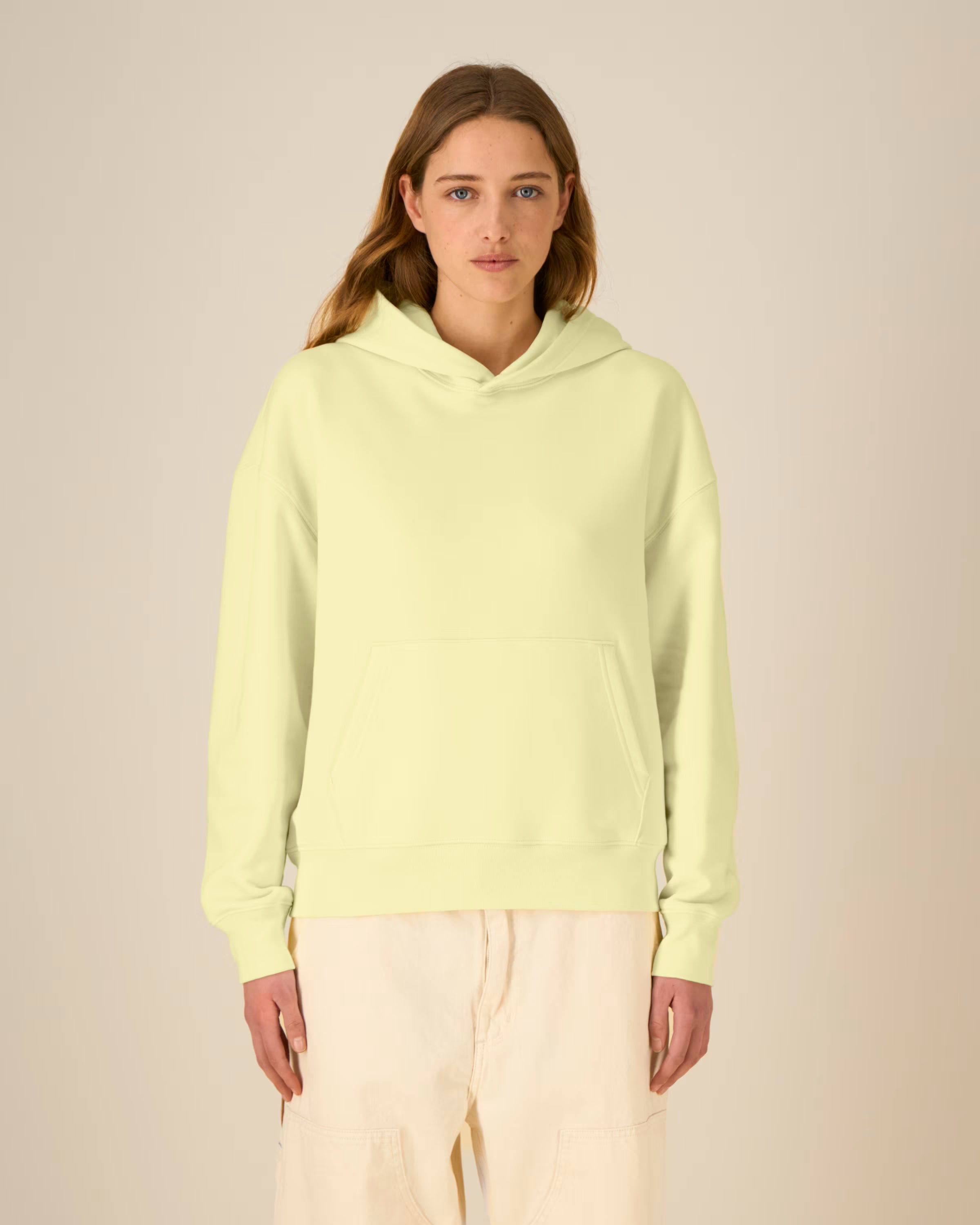 Person wearing a light green unisex cotton hoodie on a beige background