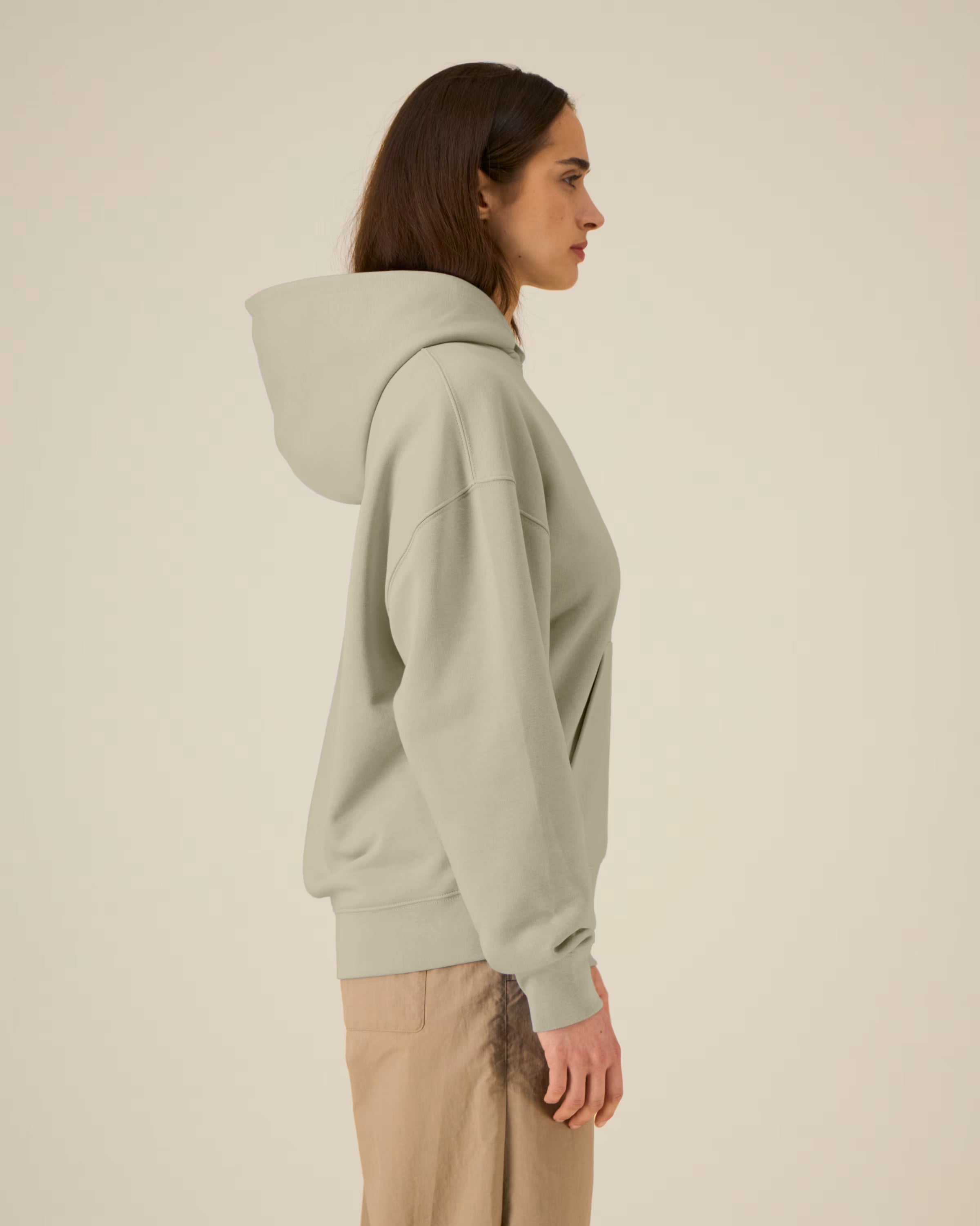 Person wearing a light gray unisex cotton hoodie and beige pants on a beige background