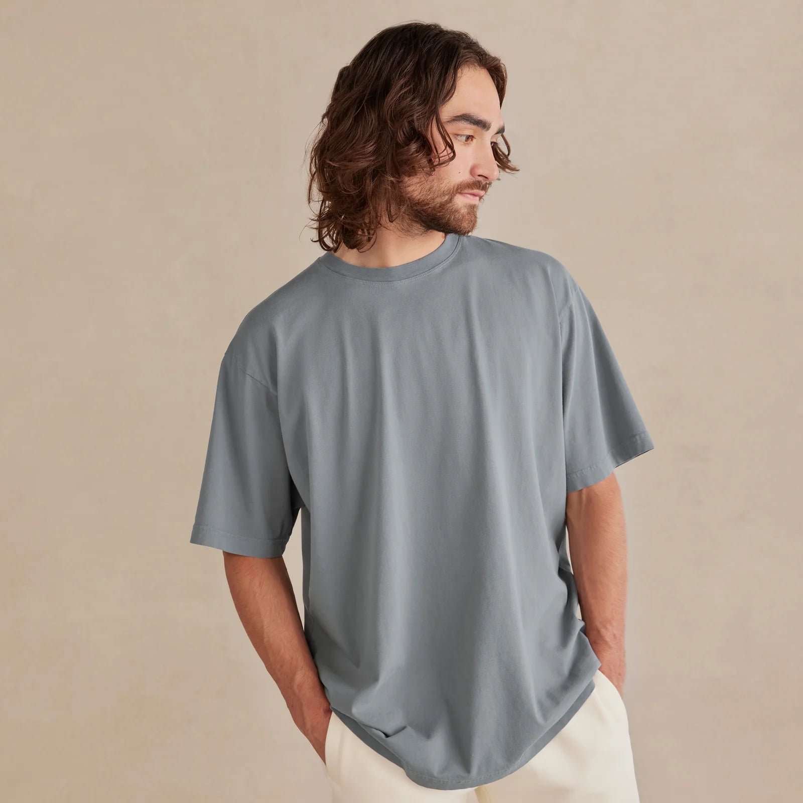Man wearing a gray  unisex cotton t-shirt against a beige background