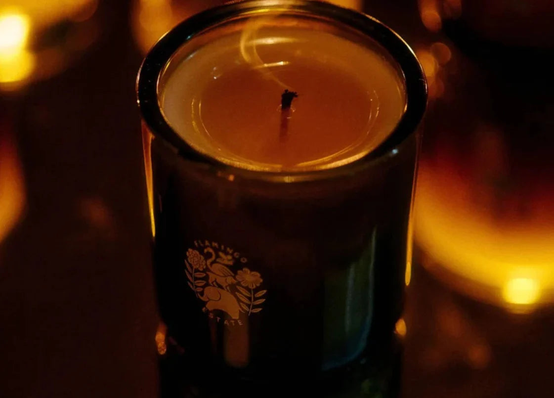 Candle in a black container with a logo, surrounded by warm glow