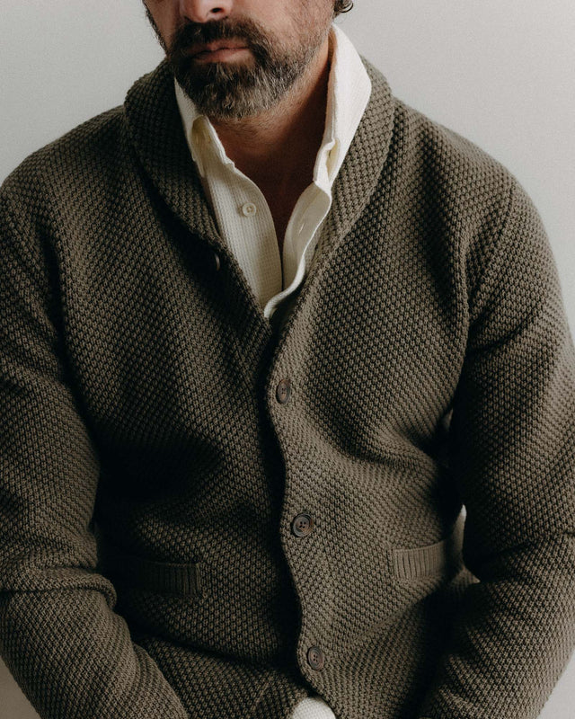 Man wearing a brown knitted cardigan over a white shirt against a neutral background